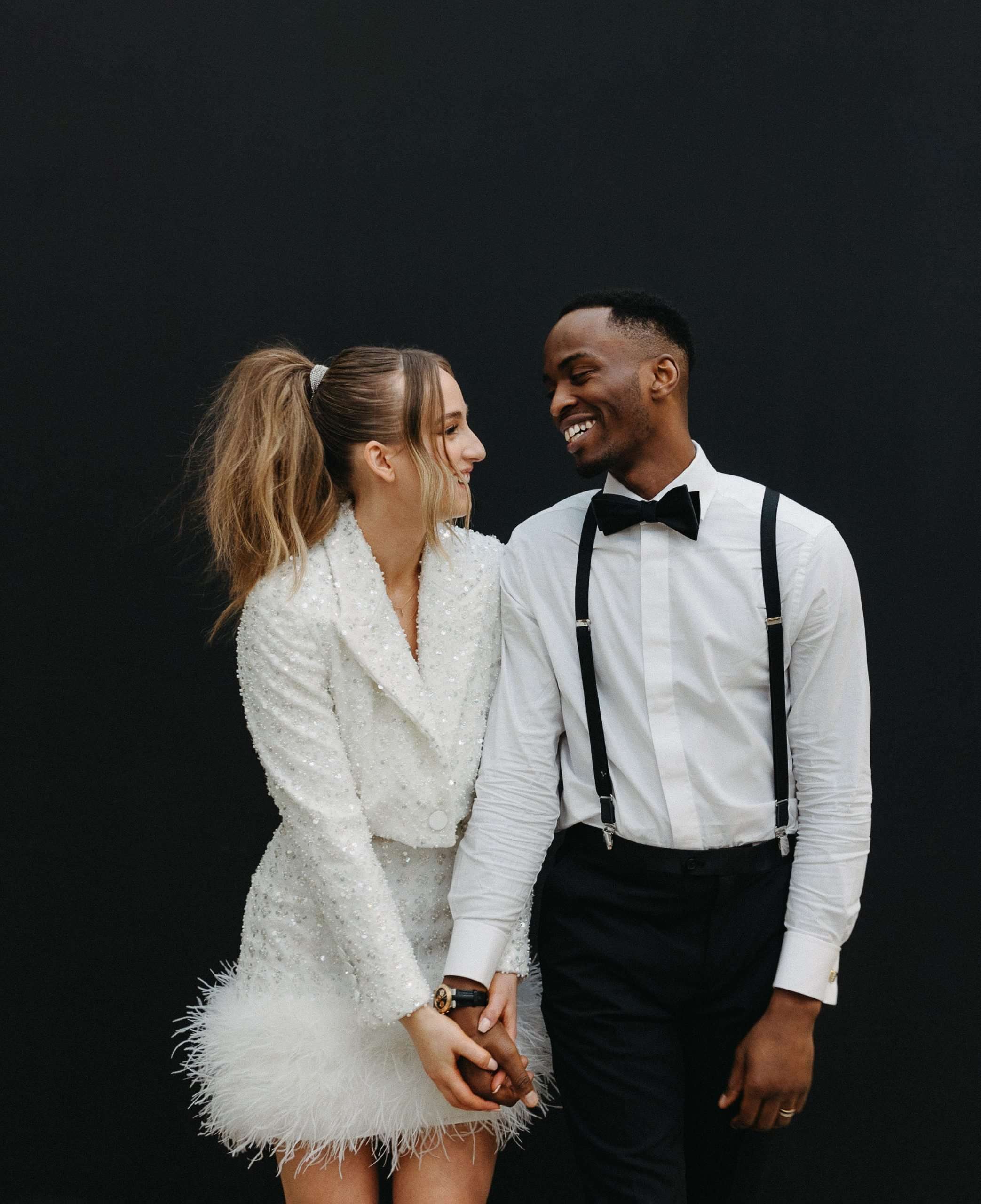 bride in white blazer and feather skirt and groom in suspenders and suit