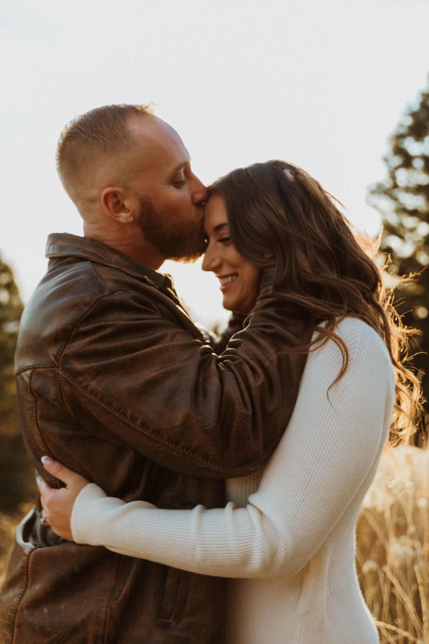 arms wrapped around his waist as he kisses her forehead for their Boise Idaho Winter Engagement Session