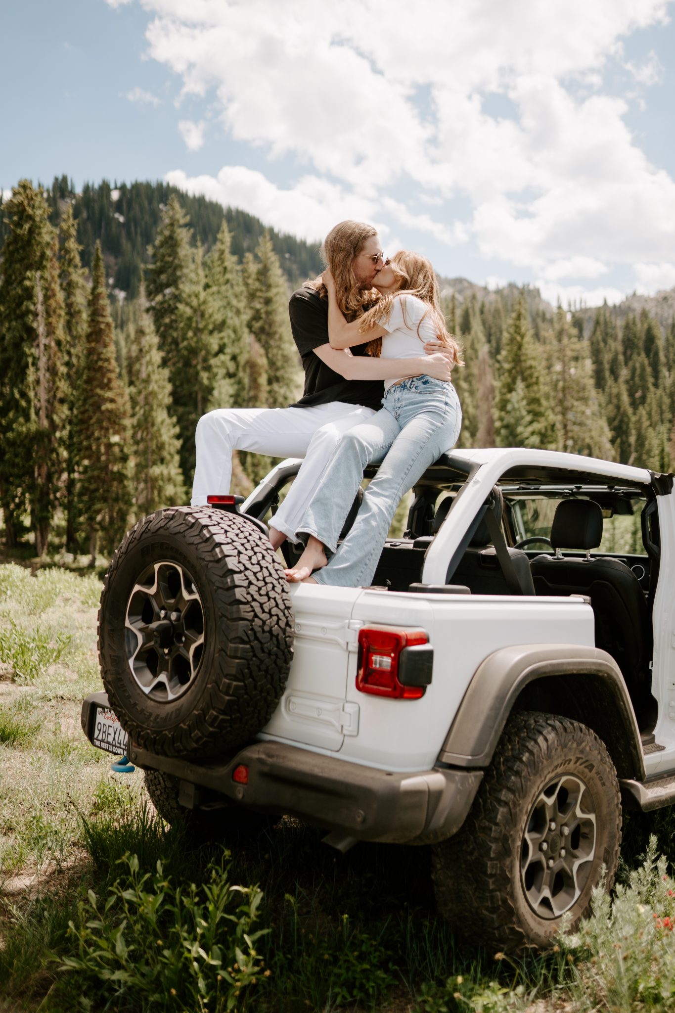 Mountain Utah Engagement Session with tree backdrop standing on the back of the jeep