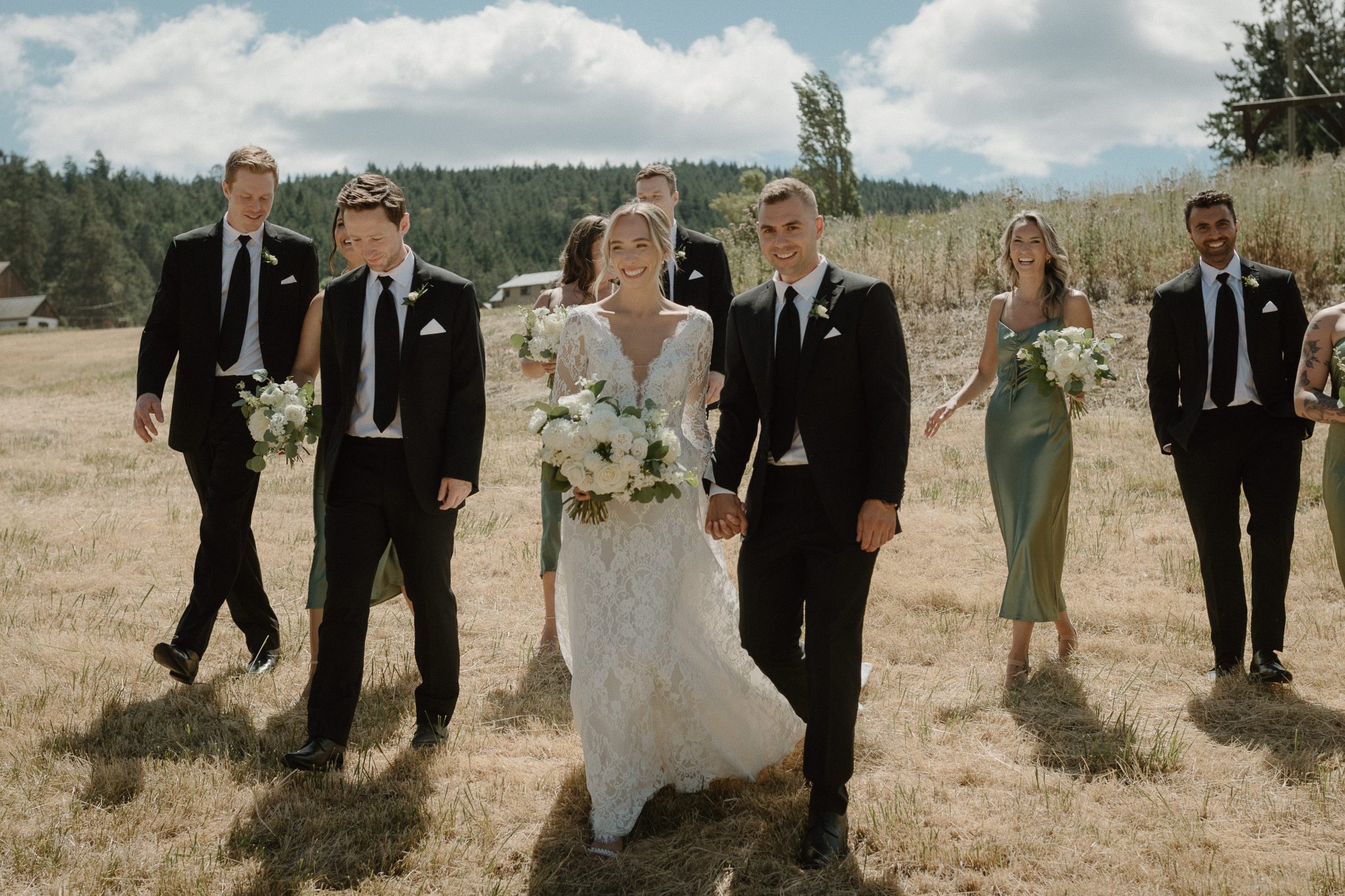 bridesmaids in green dresses and groomsmen in black suits walking through the grass for a White and Green British Columbia Summer Wedding