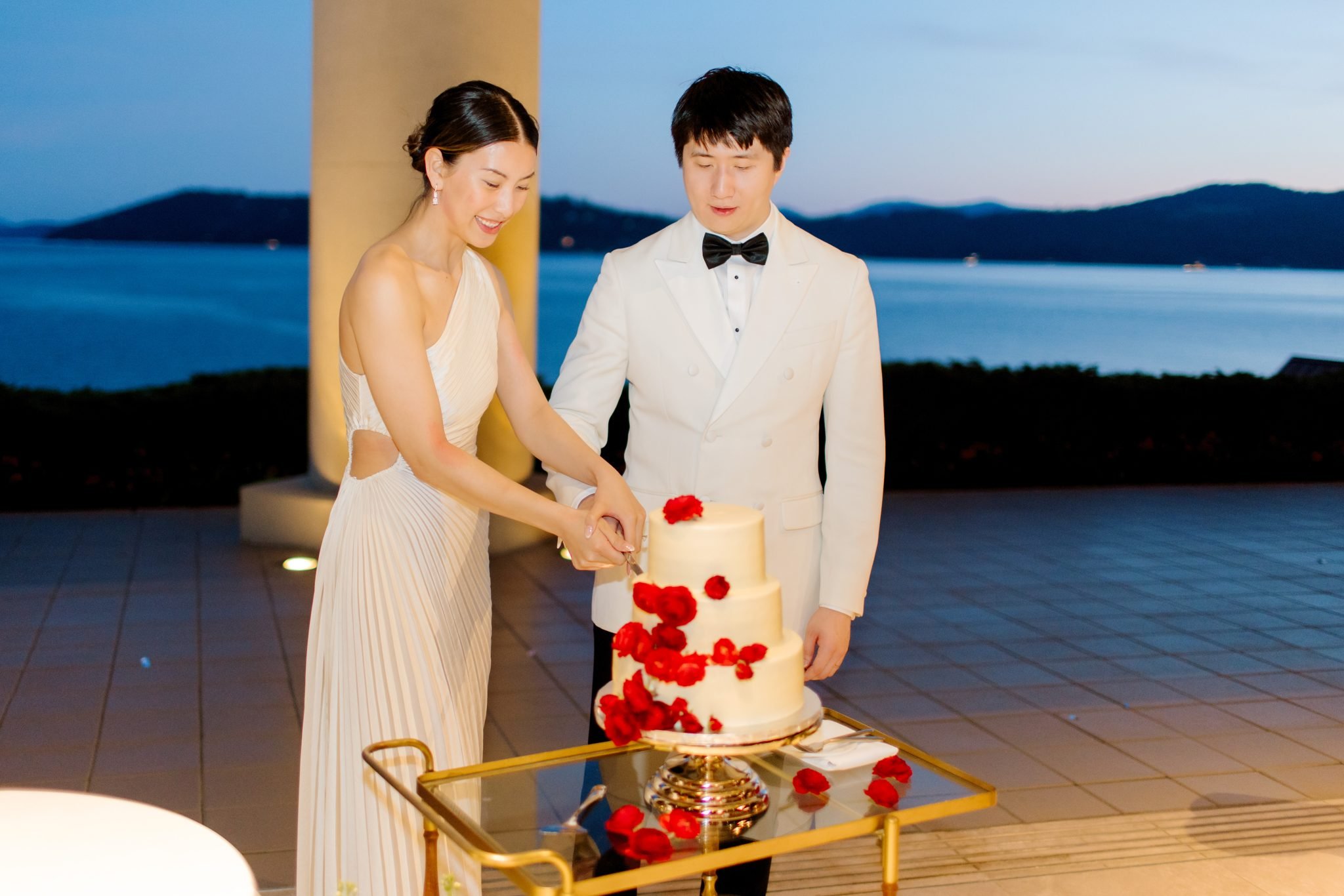 idaho summer wedding couple cutting into their white wedding cake that has red flowers