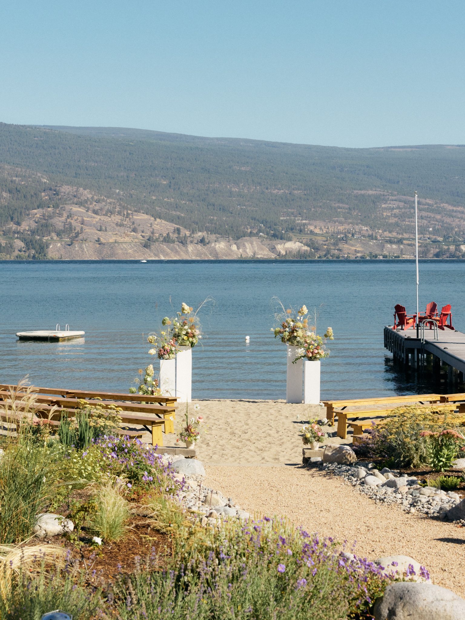 Lake and mountain backdrop for ceremony with benches for guest seating and and ceremony floral pieces to frame the couple for their British Columbia Summer Wedding