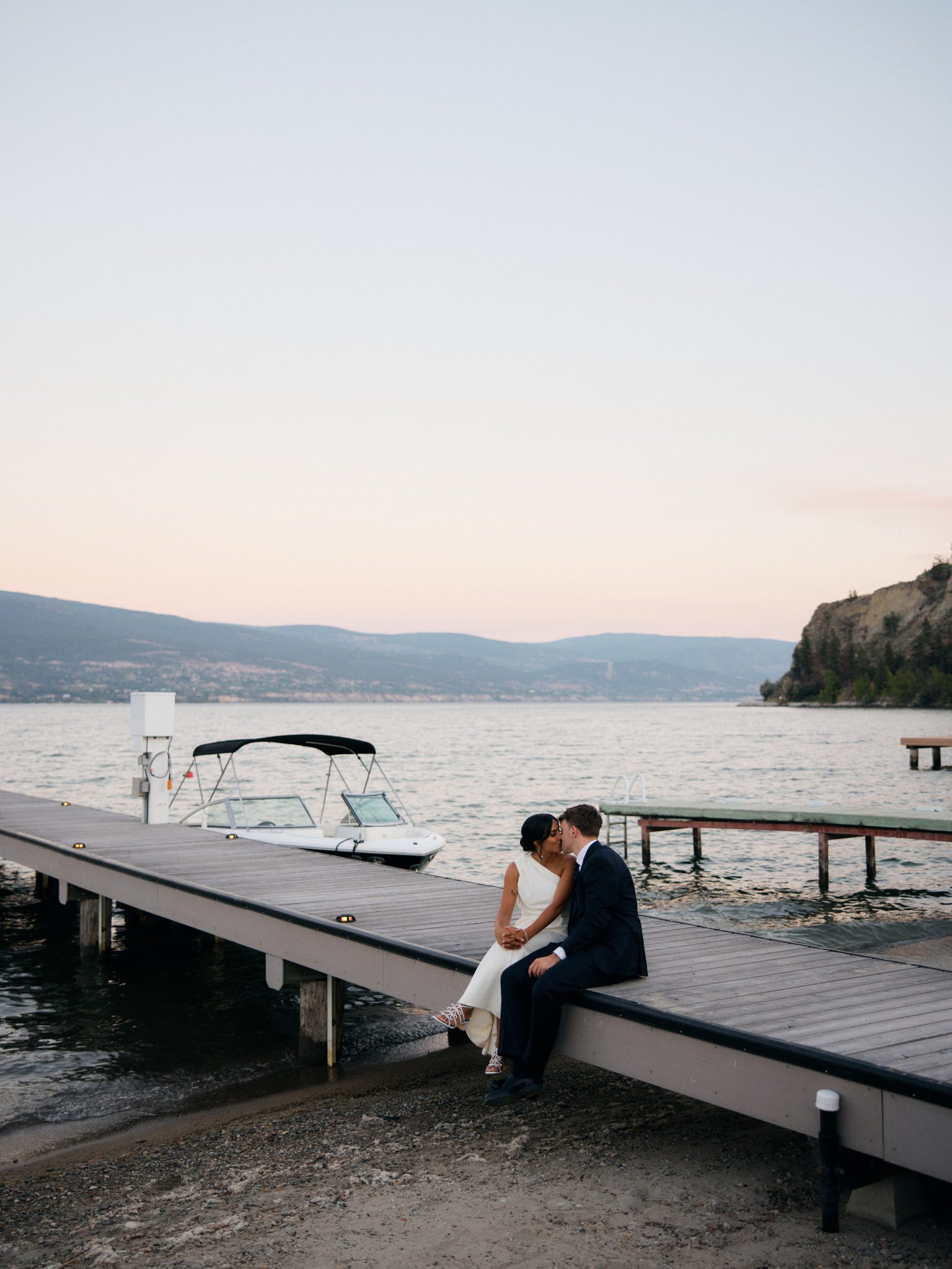 Bride and groom take sunset photos on the dock with mountain views in the background for their British Columbia Summer Wedding