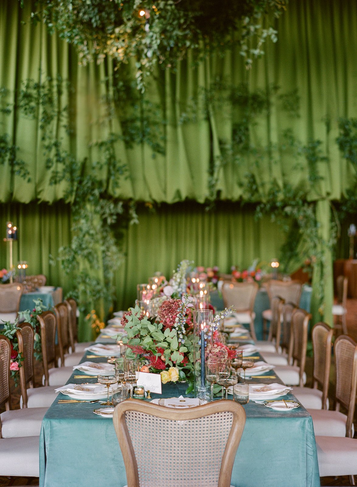 Stunning reception area with hanging greenery, green drapery, greenery cascading on the walls, and beautiful banquet tables with florals and candles for a Broadmoor Fall Wedding