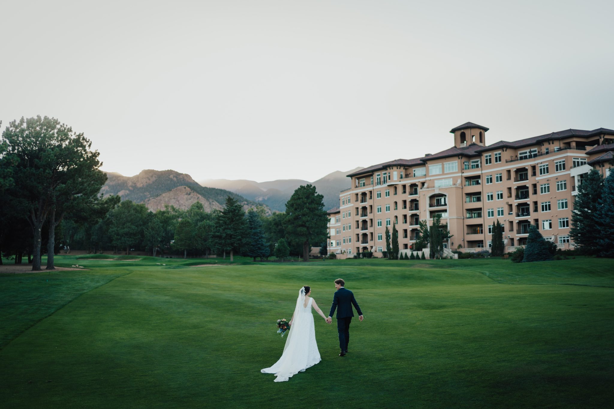 Bride and groom holding hands walking across the Broadmoor's golf course for their Broadmoor Fall Wedding