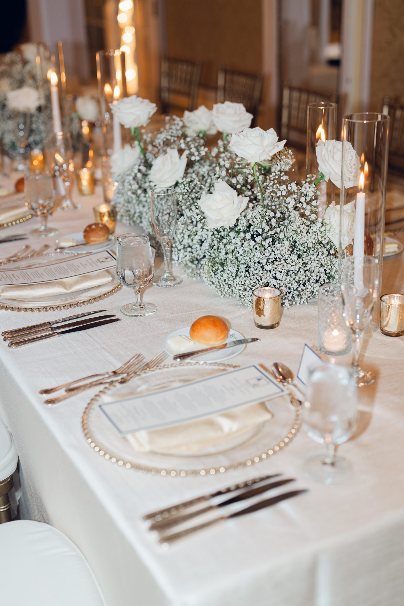 Colorado Springs Summer Wedding reception table with tapered candles, gold votive candles, gold rimmed chargers, and white roses and baby's breath floral arrangements