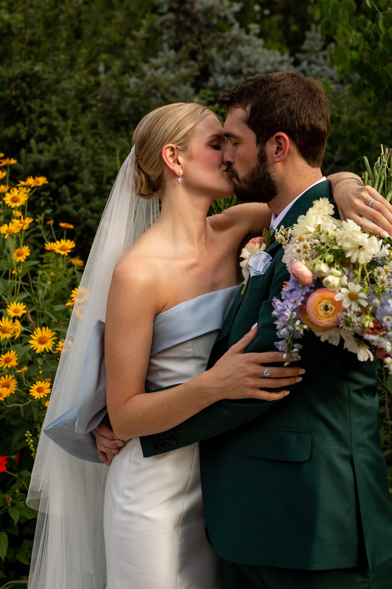 Denver Botanic Gardens Colorado Wedding bride and groom kissing in the gardens as the bride wraps her arm around the groom's back while holding her colorful bouquet
