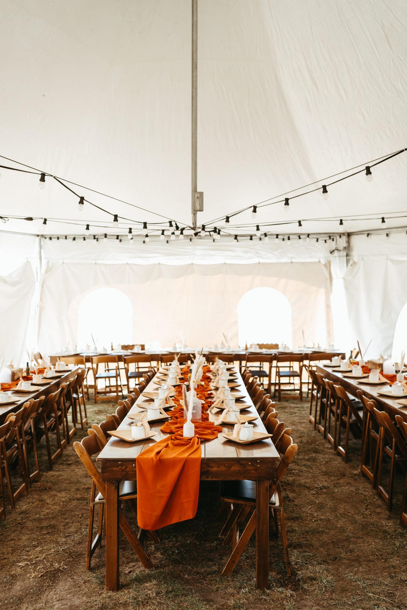 Colorado Fall Wedding reception area under a tent with wooden banquet tables and an orange runner down the middle of the table