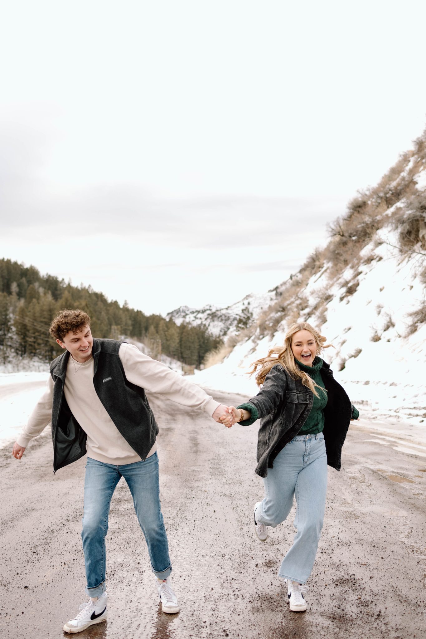 Idaho Winter Engagements couple running through the road with snow backdrop and evergreen trees