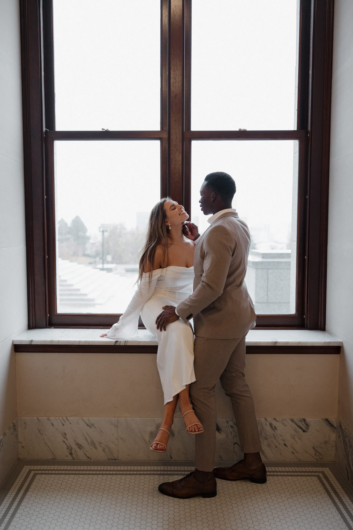 Bride sitting on the ledge as groom gently holds her face in front of a window for Utah wedding bridals