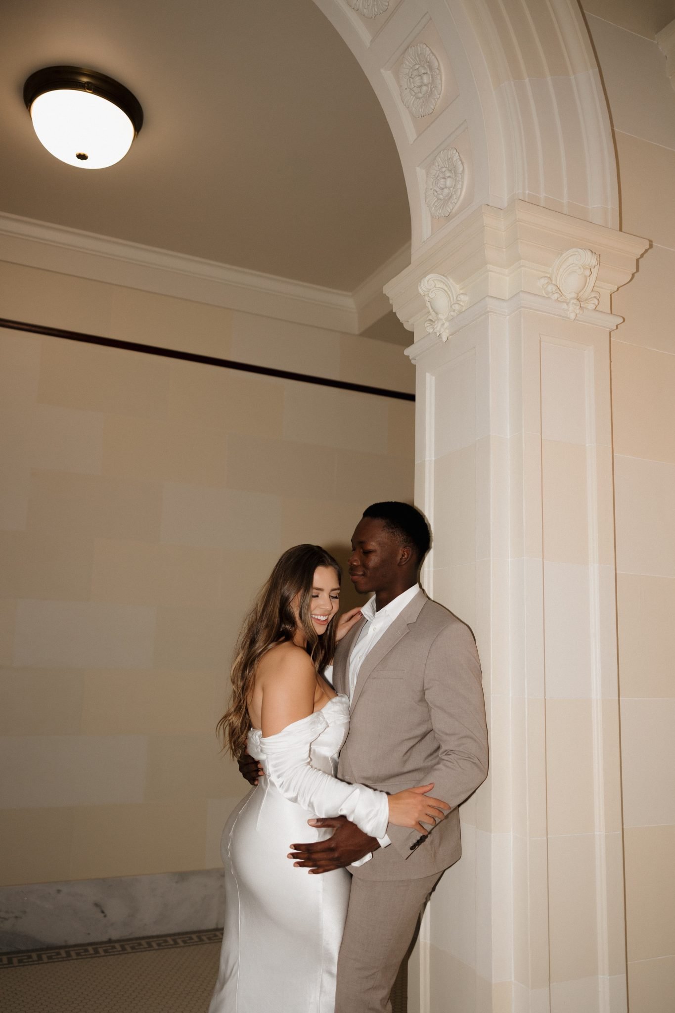 Bride and groom leaning against the wall for Utah wedding bridals as she wears a silk floor length dress and he wears a gray suit