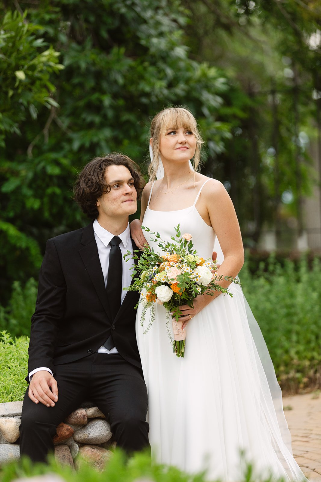Highlands Ranch Summer Wedding groom in his black suit and the bride wearing her white chiffon wedding dress while holding her wedding bouquet with white and orange florals