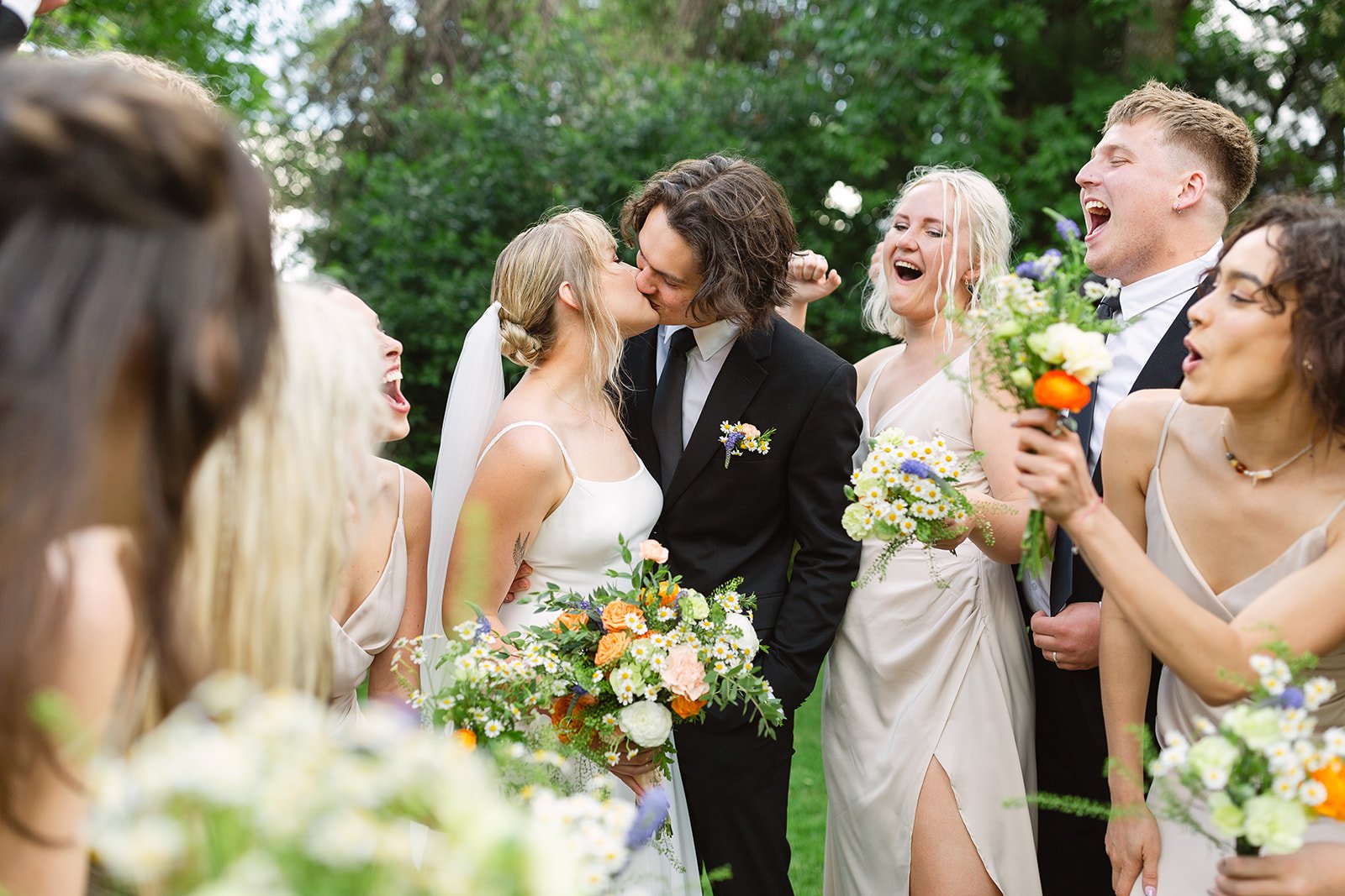 Highlands Ranch Summer Wedding couple kissing as they are surrounded by their bridal party as they cheer