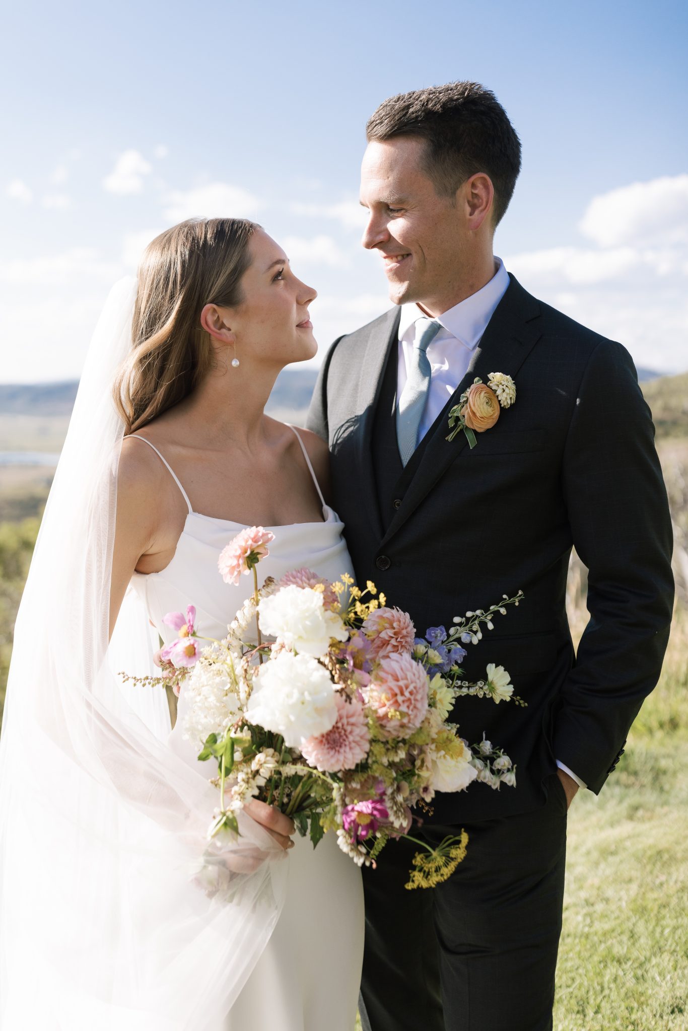 bride and groom looking at one another as the bride holds her pink, purple, and white bouquet as she wears a simple but elegant wedding dress with a veil for a Steamboat Springs Summer Wedding