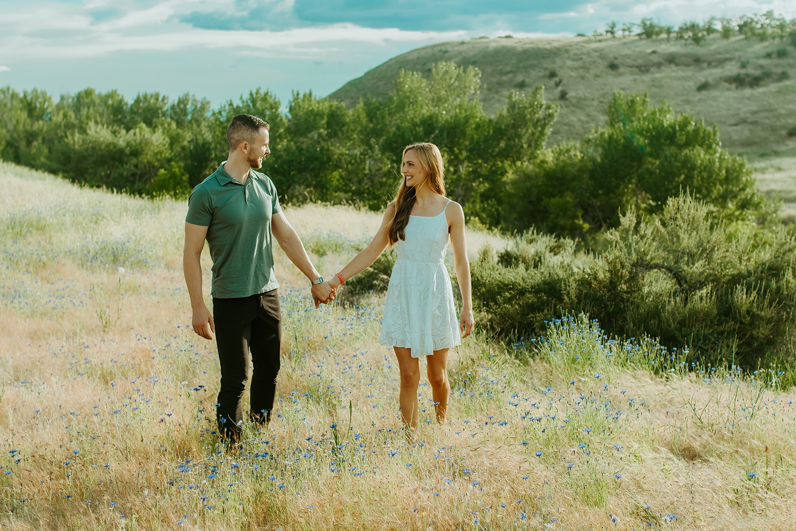 Idaho Summer Engagement Session couple holding hands in a field as they look into each others eyes and smile