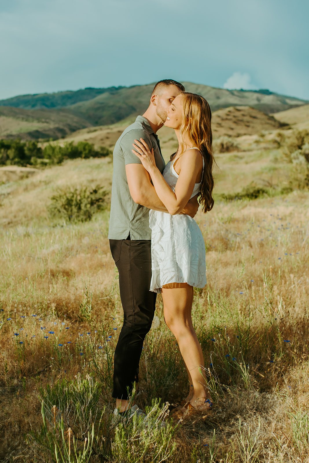 He kisses her cheek in a meadow with cute matching outfits Idaho Summer Engagement Session