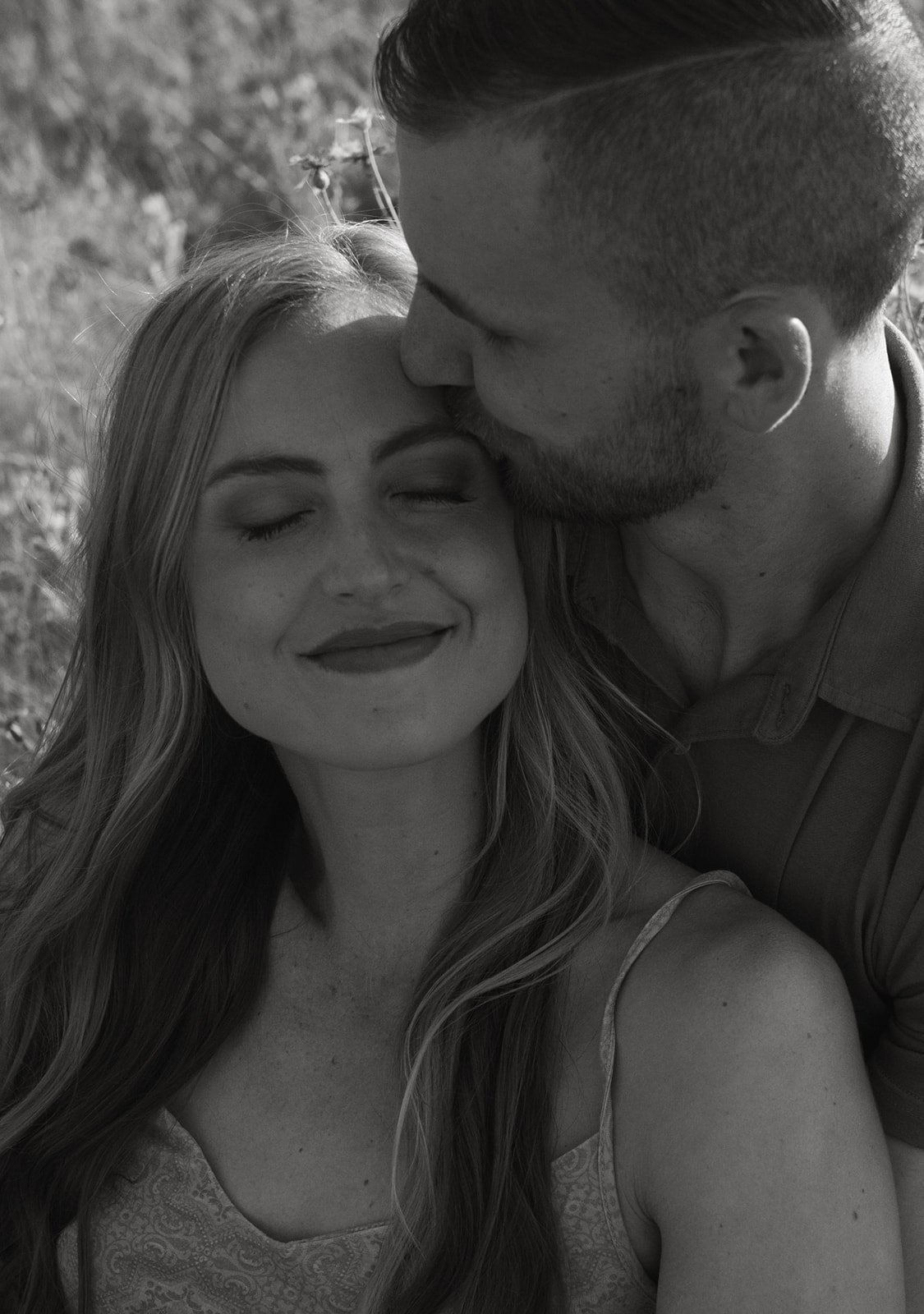 Idaho Summer Engagement Session couple sitting in the meadow as he kisses her temple and she soaks in the moment