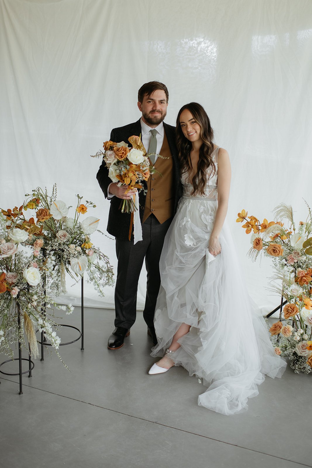 bride and groom posing at their ceremony altar with medium height white and orange floral colors as the bride wears a tool wedding dress for their Summer whistler wedding