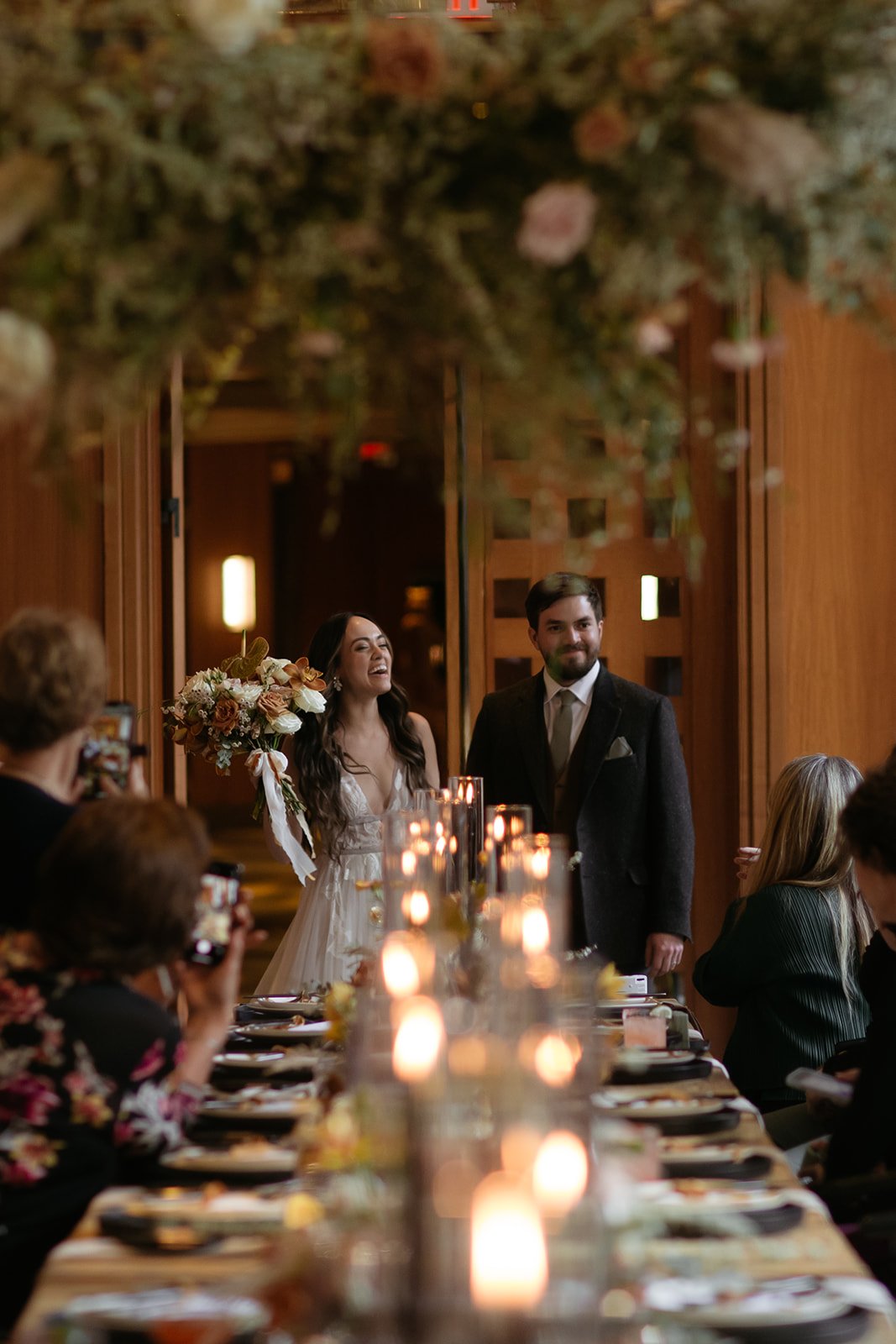 bride and groom having their grand entrance into their reception room with hanging floral arrangements and tapered candles down the reception table for their Summer whistler wedding