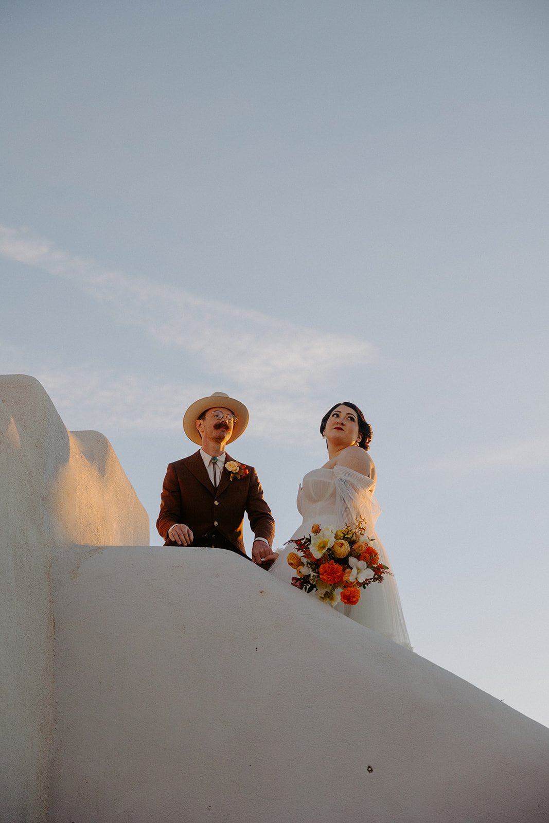 The Stakeout Taos Wedding bride wearing a stunning wedding dress as she hold her vibrant colored wedding bouquet, and the groom wearing a brown suit and stylish hat
