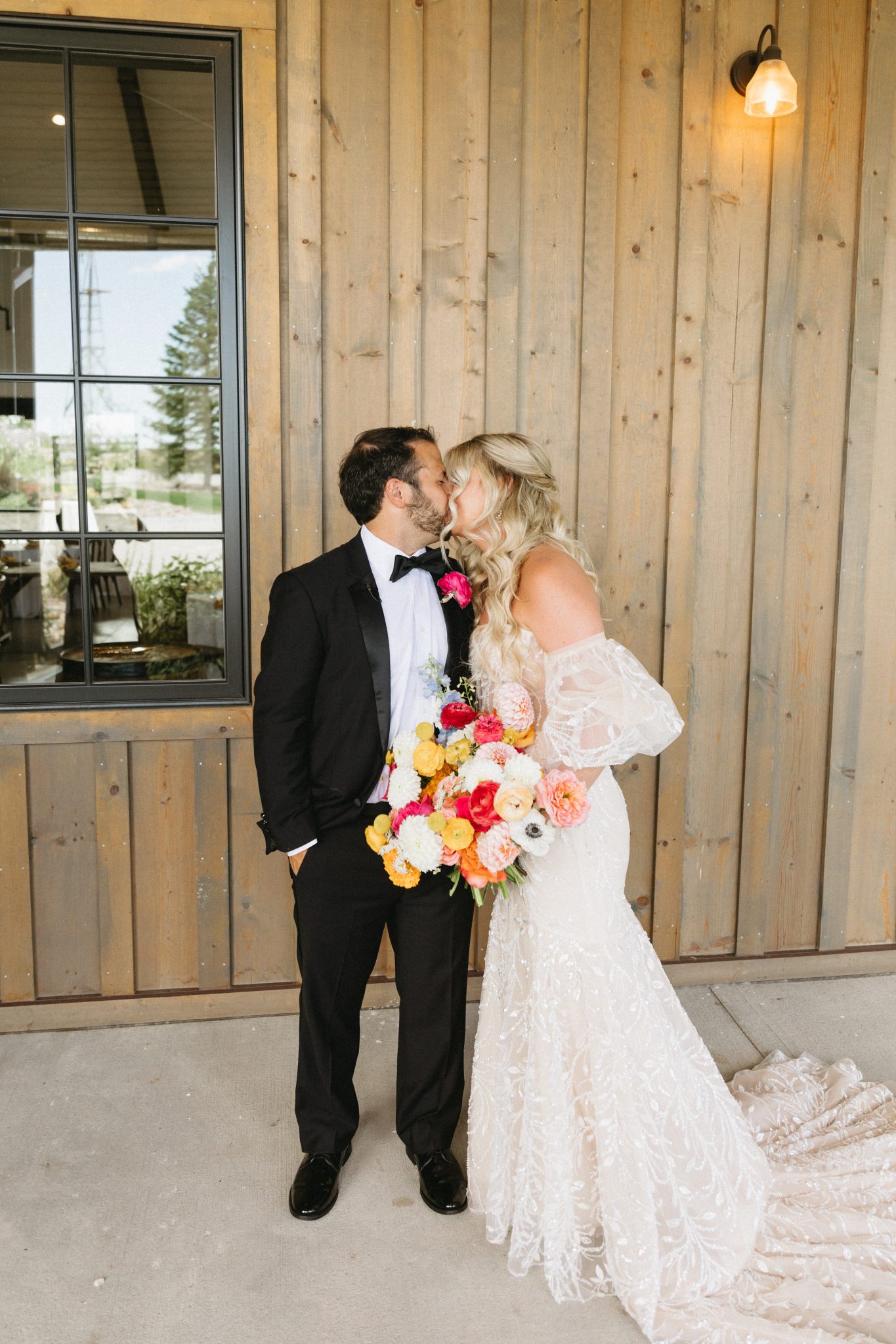 Bonnie Blue's Summer Wedding bride and groom kissing with the groom wearing a tuxedo and the bride wearing her statement wedding dress and holding her colorful and vibrant bouquet