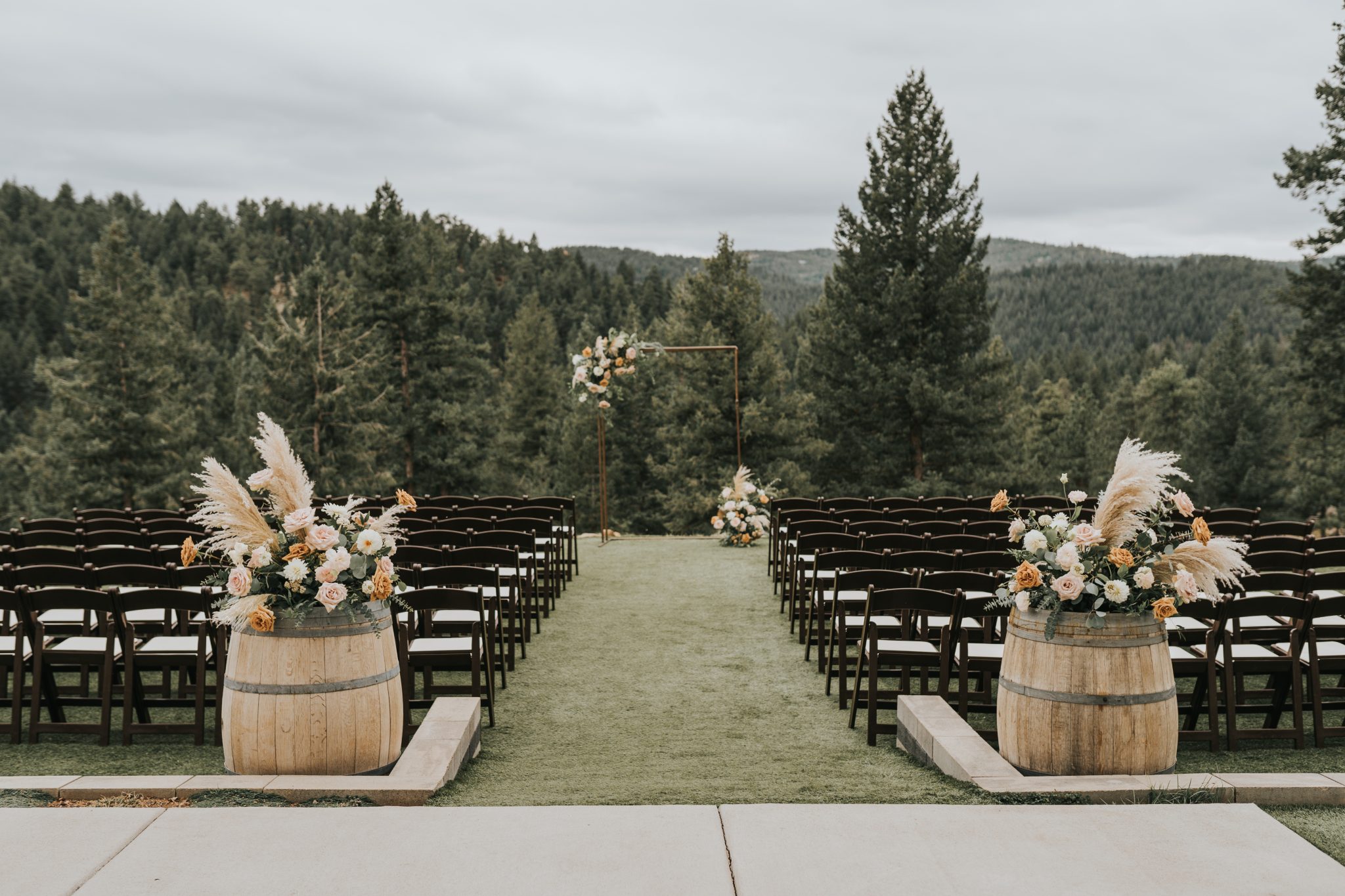An outdoor wedding ceremony setup with an aisle lined with pampas grass and floral arrangements at a Colorado Winter Woodlands Wedding.