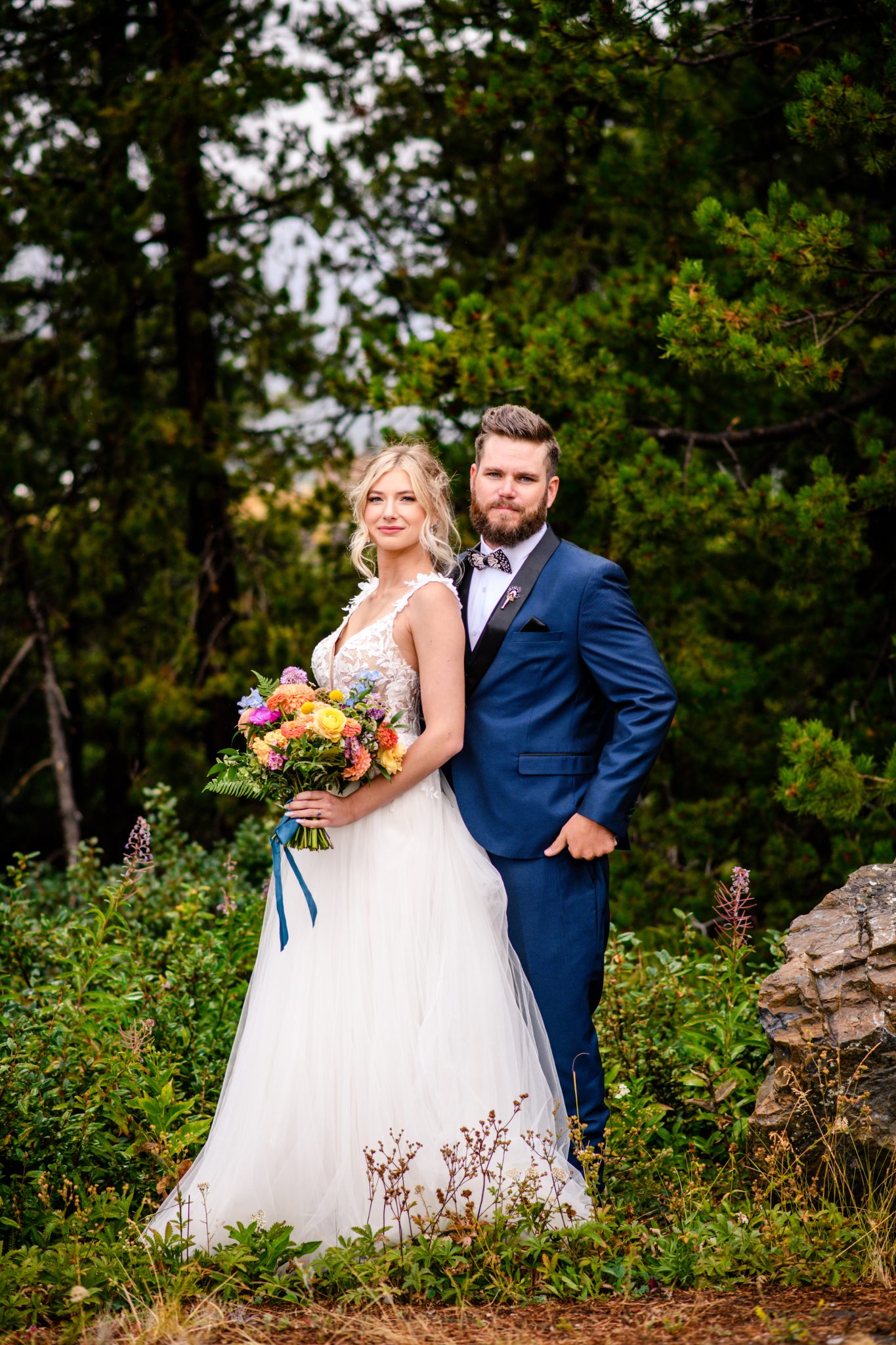 Glacier National Park Elopement couple after their first looking with the groom wearing a blue suit and the bride holding her colorful wedding bouquet