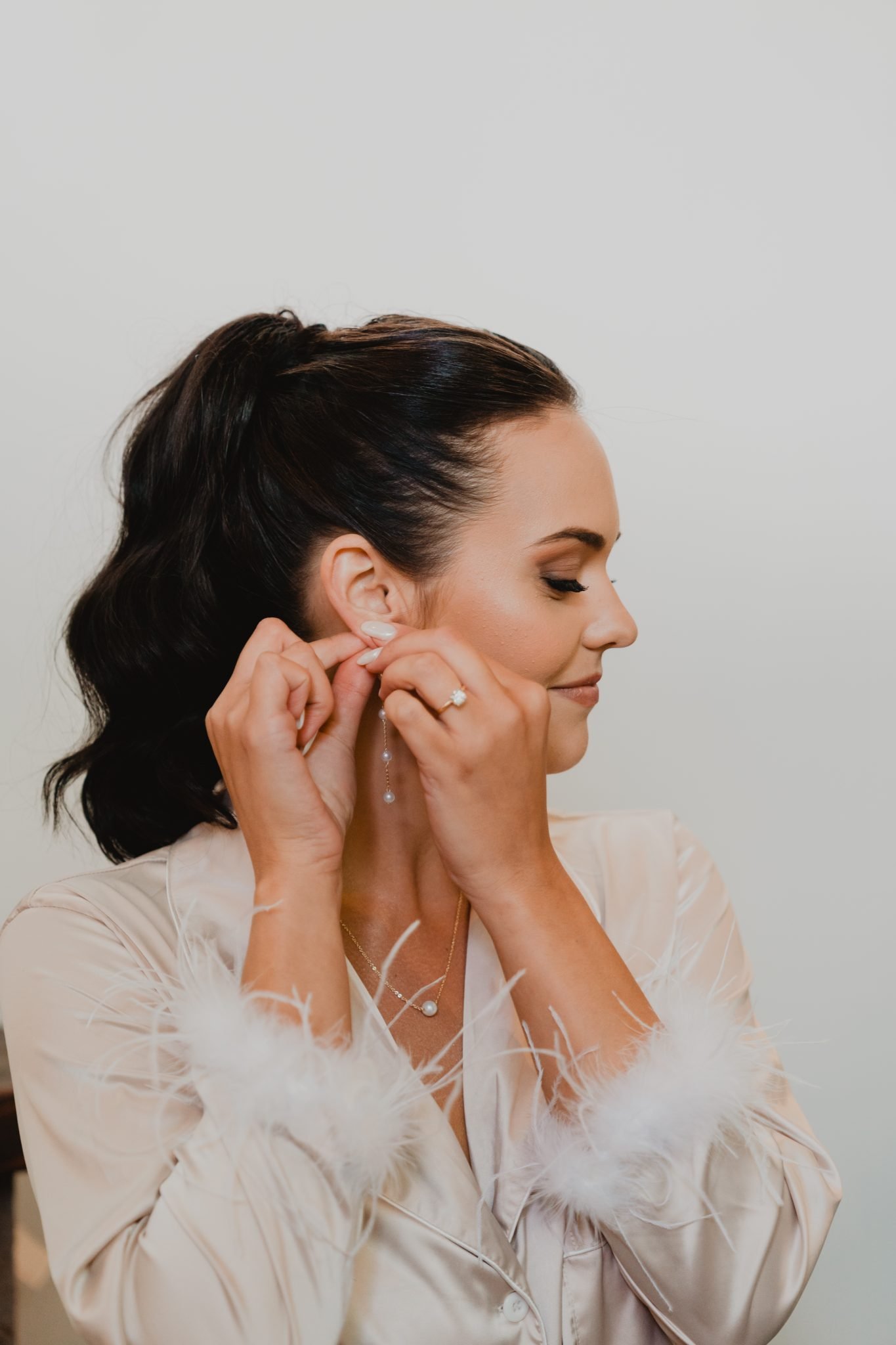 Grand Teton National Park Elopement bride putting on her dangle pearl earrings as she wears her beige pajamas with feathered sleeves