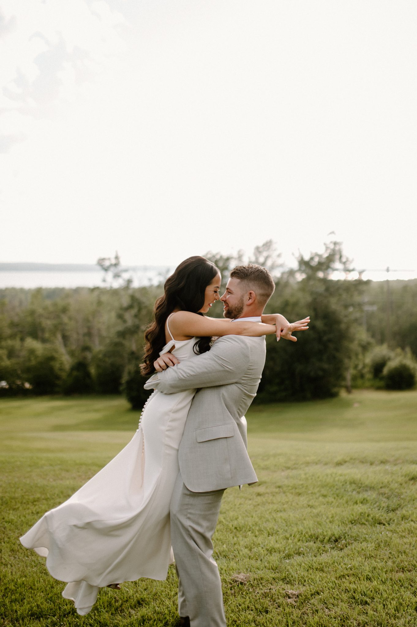 Hilltop Wedding Center Summer Wedding groom picking up the bride as she puts her hands around his neck and they smile as they look into each other's eyes