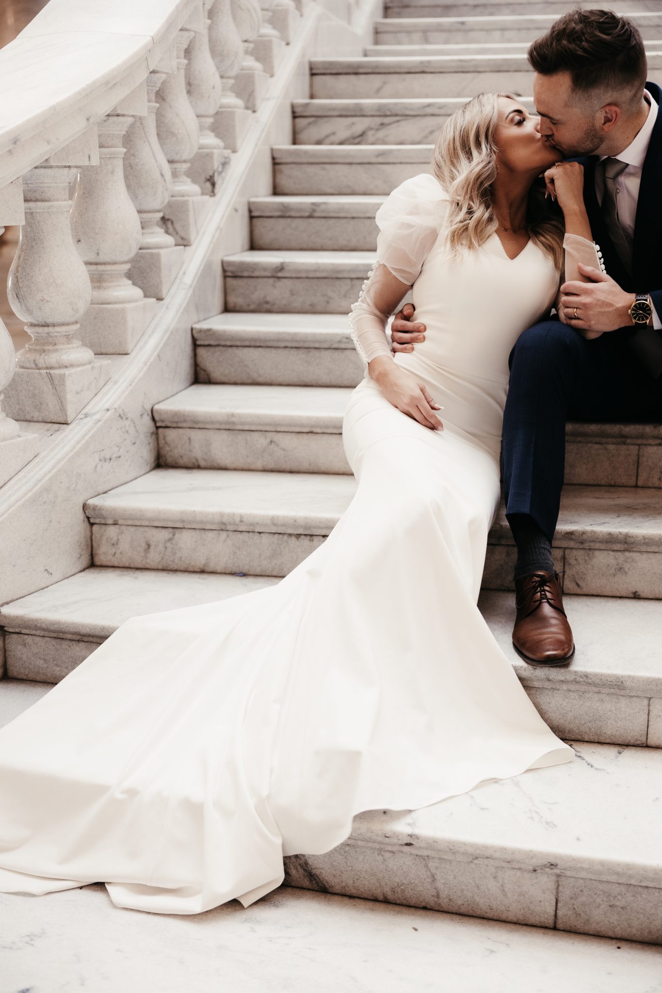 Utah Winter Engagement Session couple sitting on the stairs as they kiss in their sleek wedding attire