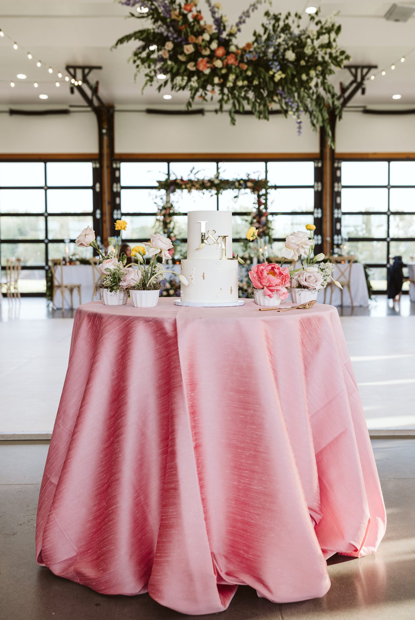Elegant white wedding cake with floral decorations on a pink table at Deer Flat Ranch Spring Wedding.