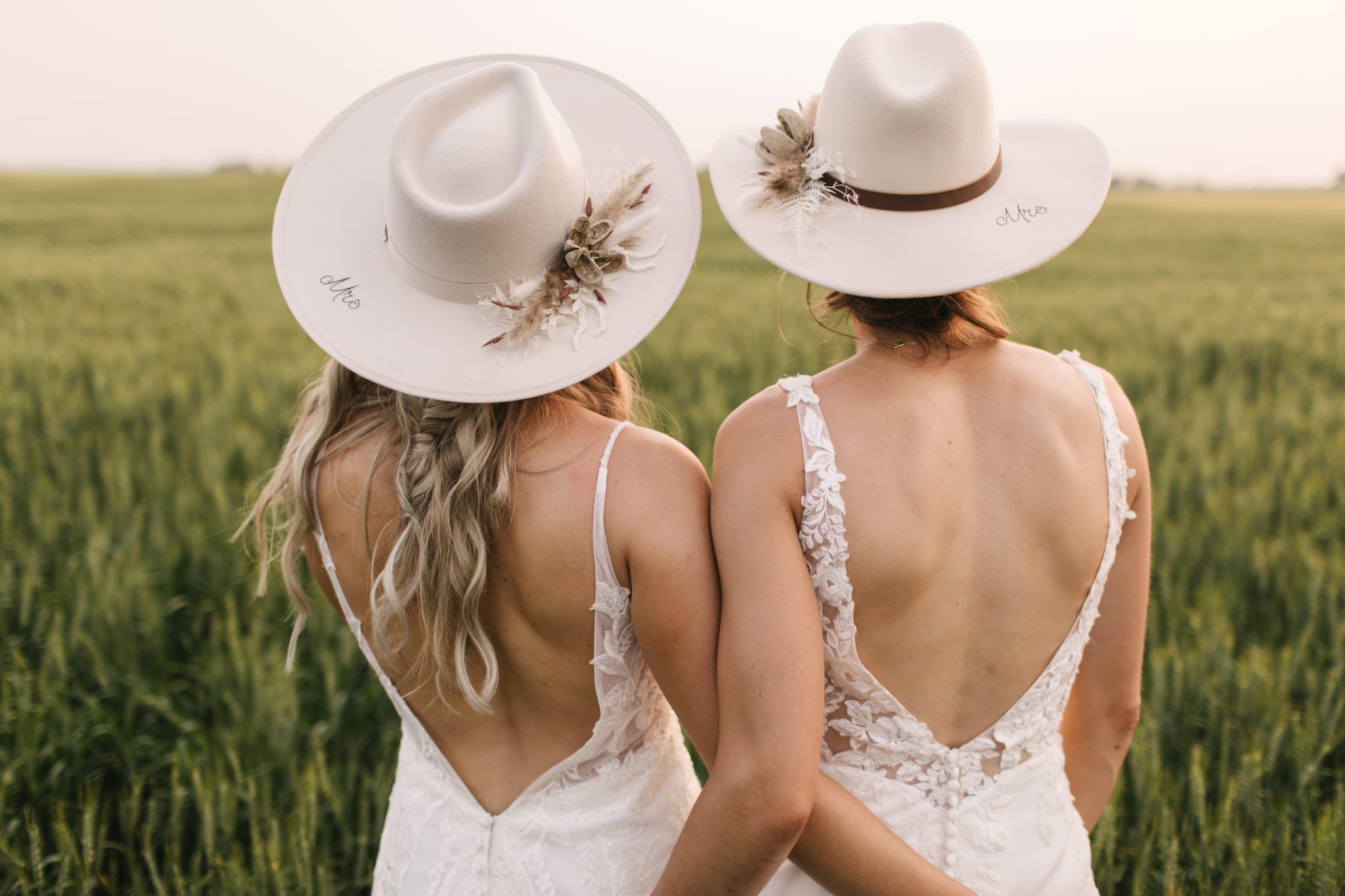 Two brides in matching hats embracing at a LGBTQIA+ Alberta Summer Wedding