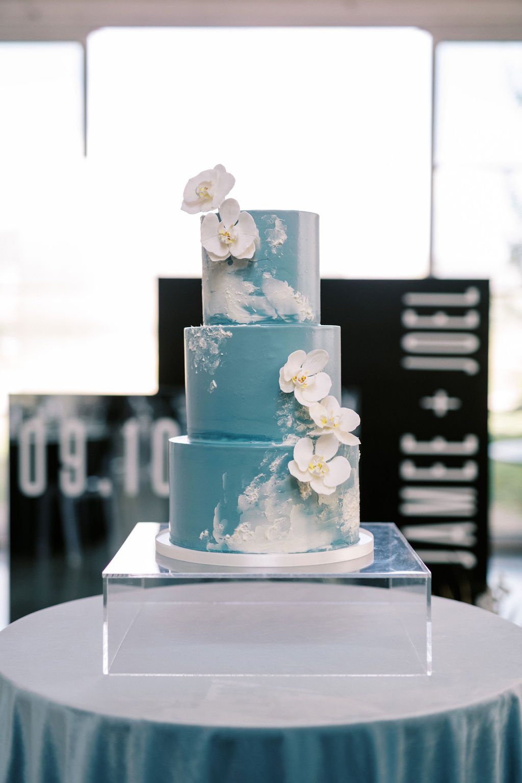 A light blue three-tier wedding cake adorned with white orchid flowers, perfect for a Peoa Spring Wedding.