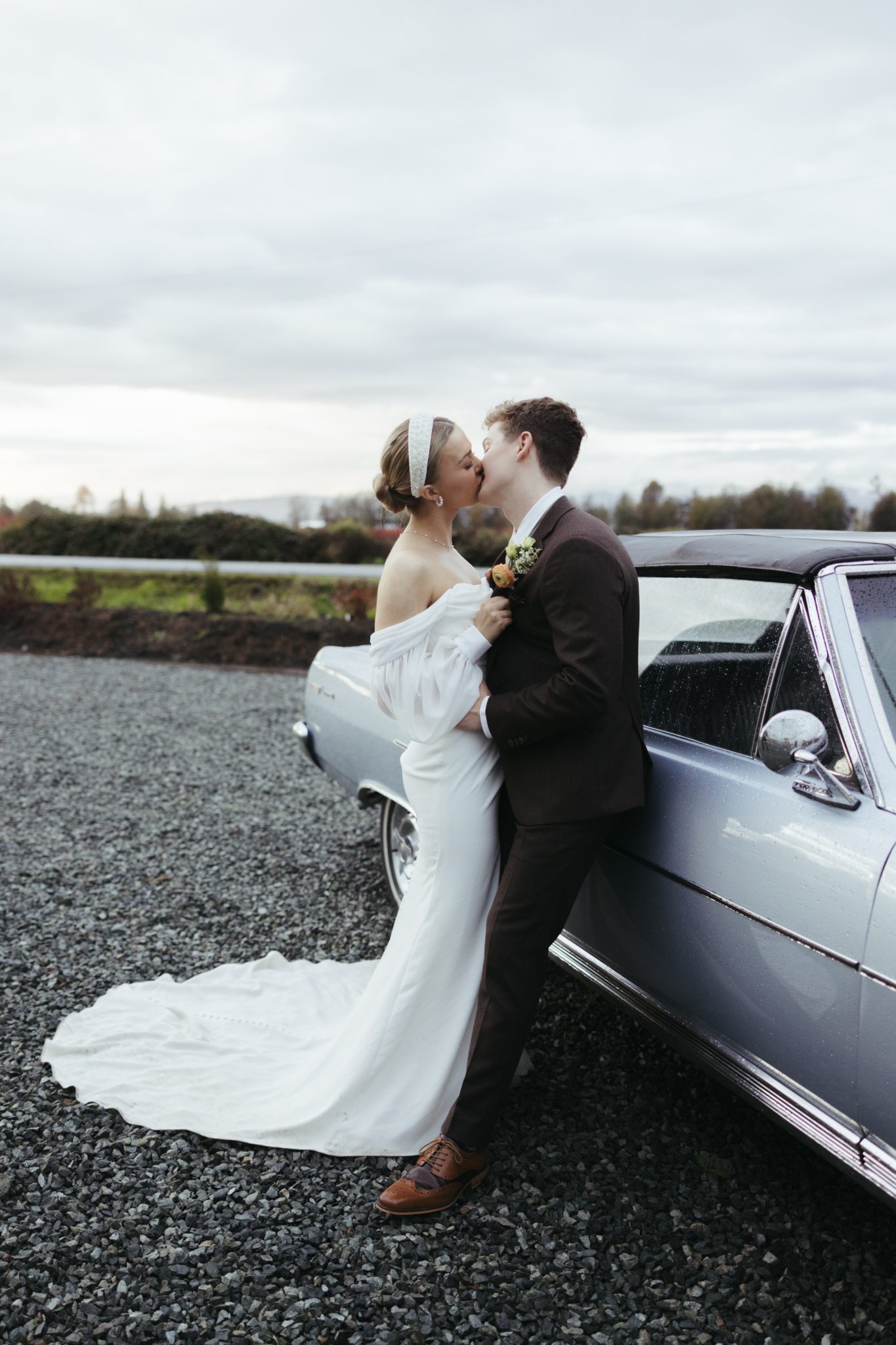Bride and groom sharing a kiss next to a classic car at their colorful British Columbia wedding.
