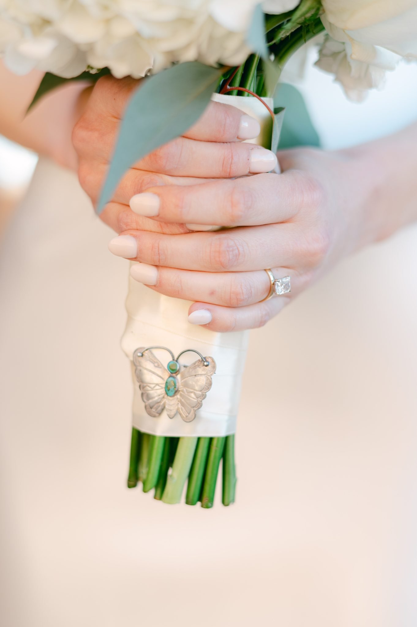 Close-up of a bride's hands holding a bouquet with a butterfly charm, perfect for a Santa Fe elopement.