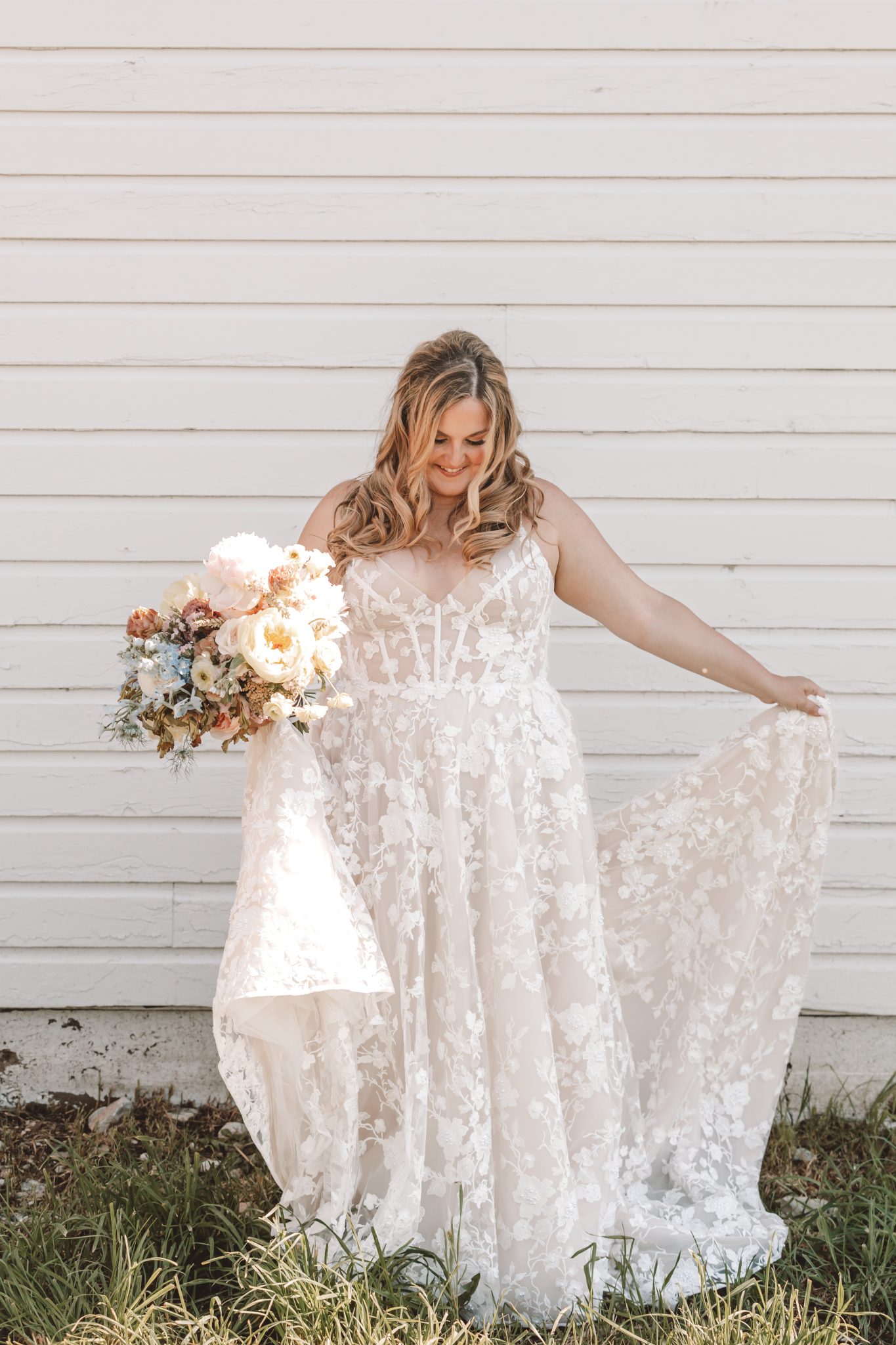Bride smiling while holding her floral bouquet in front of a white wall at a Montana Summer Wedding