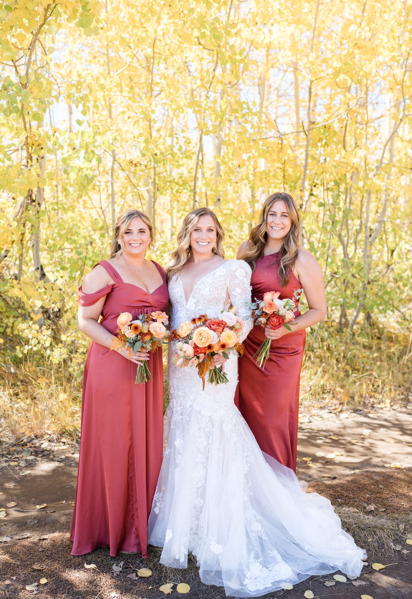 Bride and her bridesmaids in rich autumn hues standing amidst golden aspen trees during a Utah fall wedding.