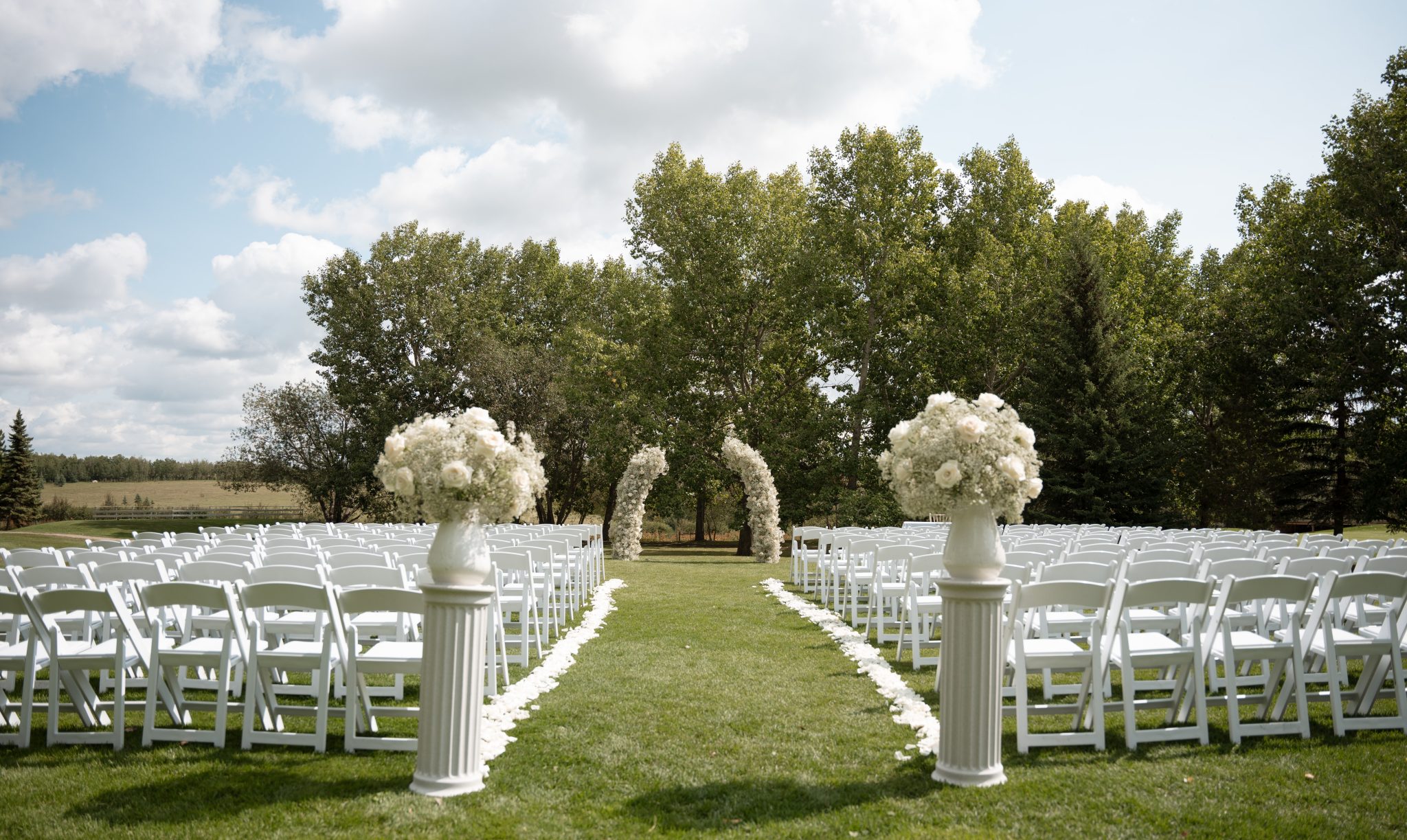 Beautiful outdoor Alberta summer wedding ceremony setup with white flowers and chairs.