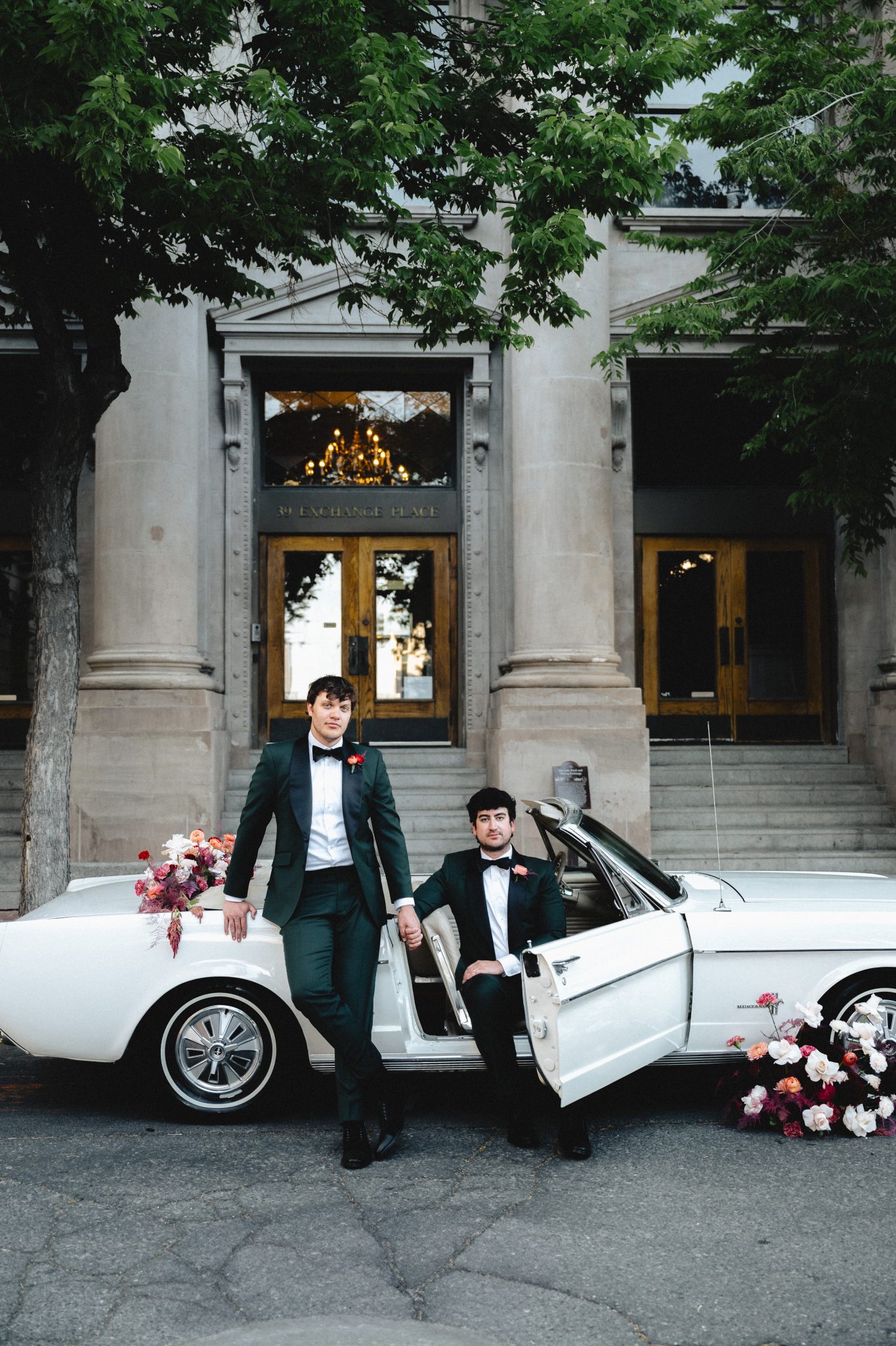 Elegant grooms posing beside a vintage white Mustang in front of a classic Salt Lake City building - Salt Lake City Wedding Inspiration.