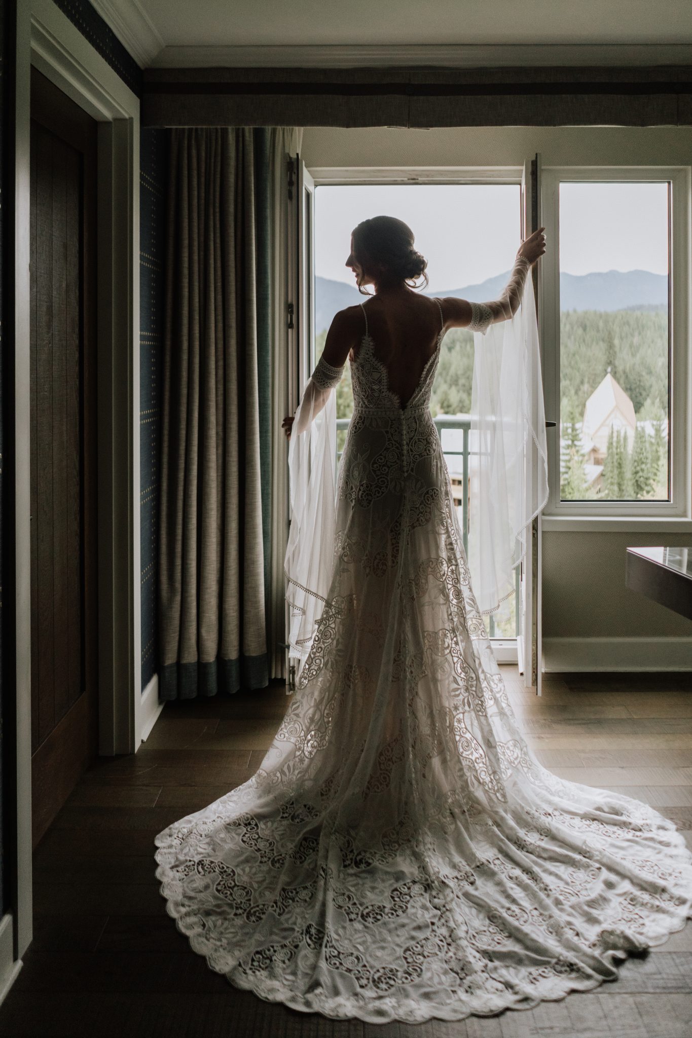 Bride in lace wedding gown standing by the window at her Whistler summer wedding.