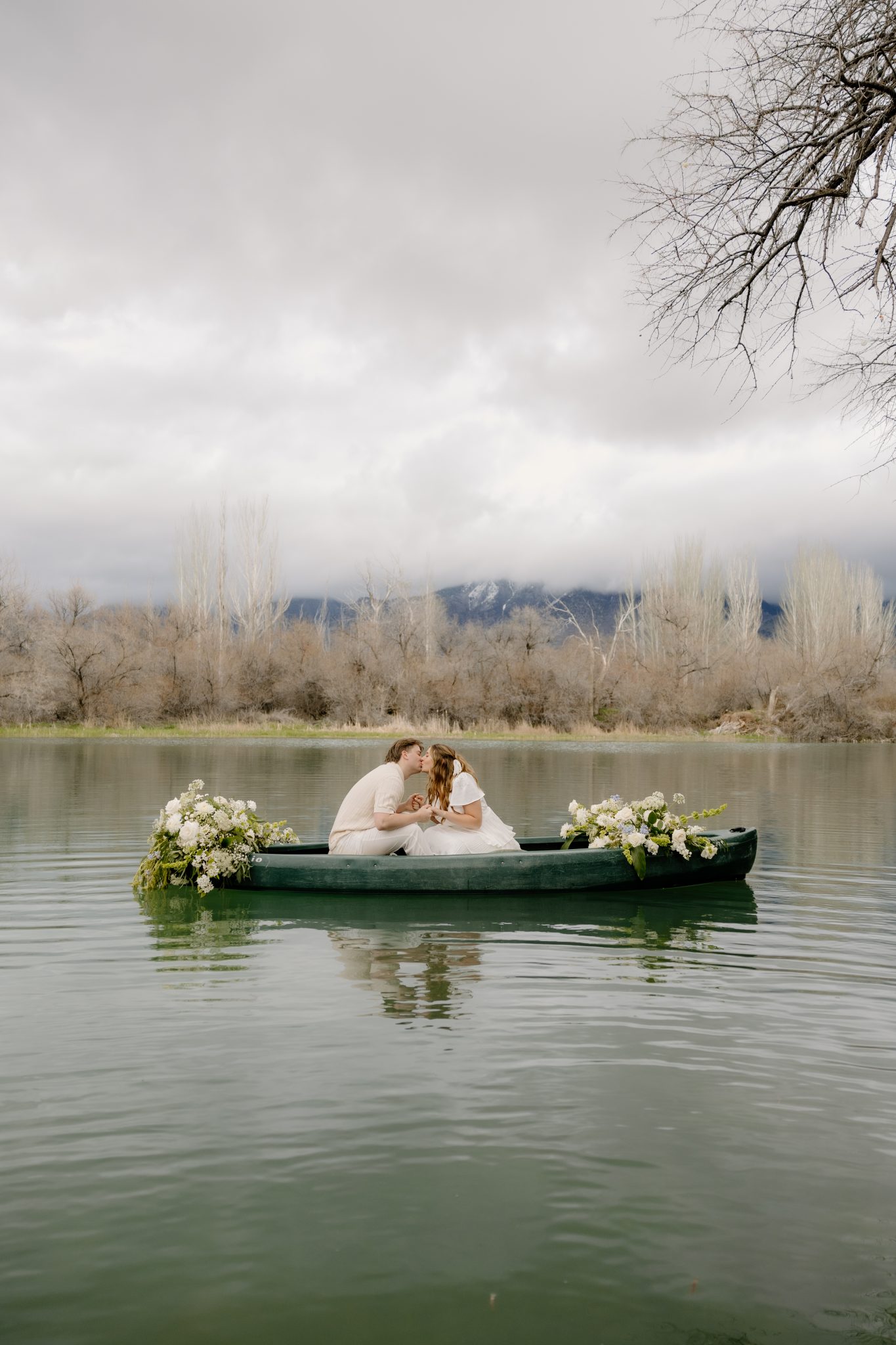 Romantic T Beebe Photo Engagement Session with the couple sharing a kiss in a canoe, beautifully adorned with white floral arrangements.