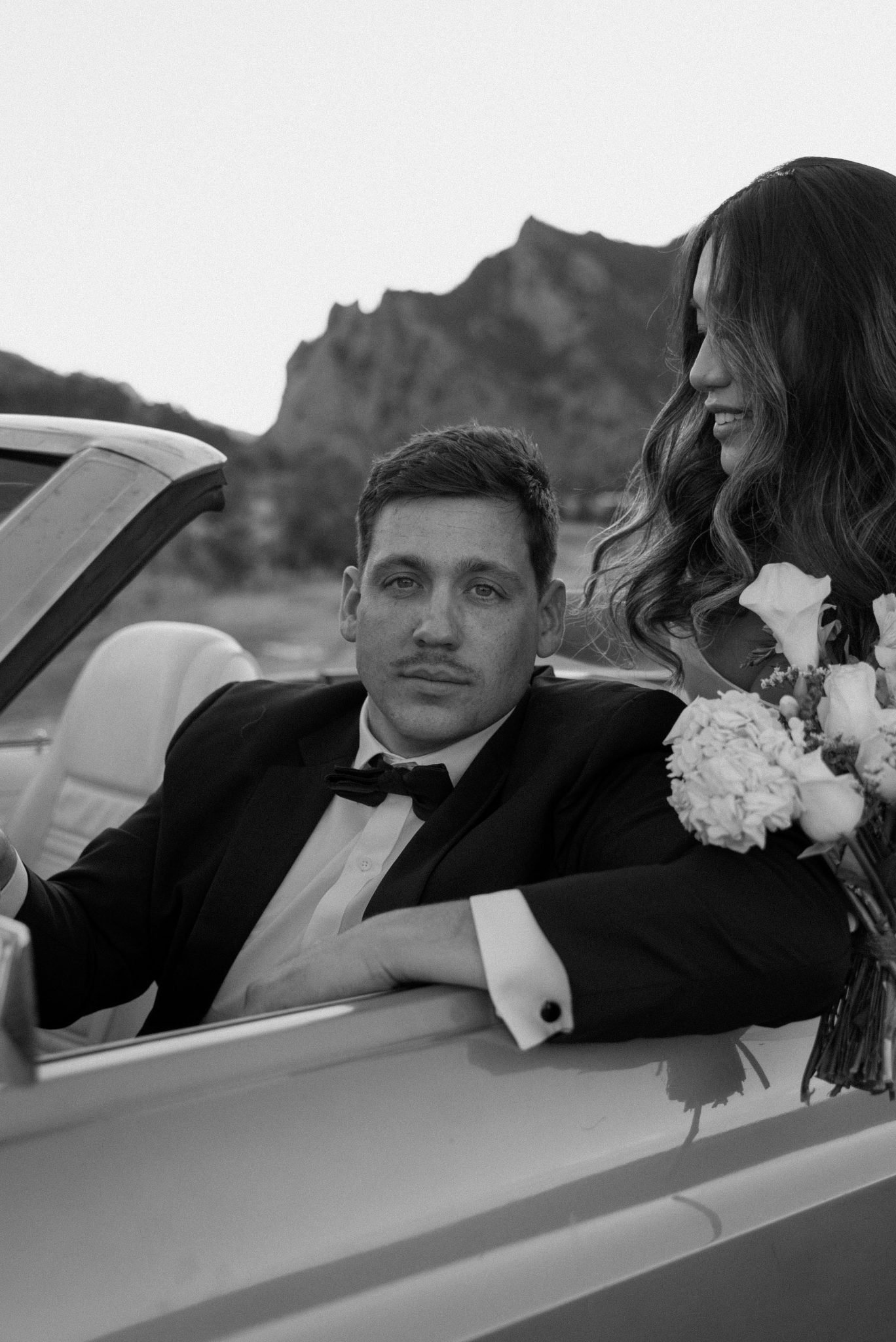 Close-up of a groom in a tuxedo and bride in a convertible during a Boulder engagement session.