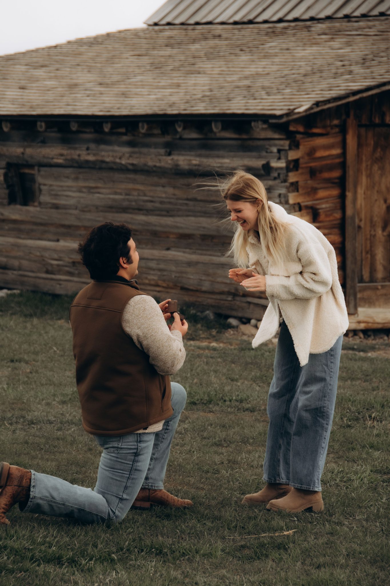 Girlfriend in surprise and joy as her boyfriend proposes in front of a rustic barn in Wyoming.
