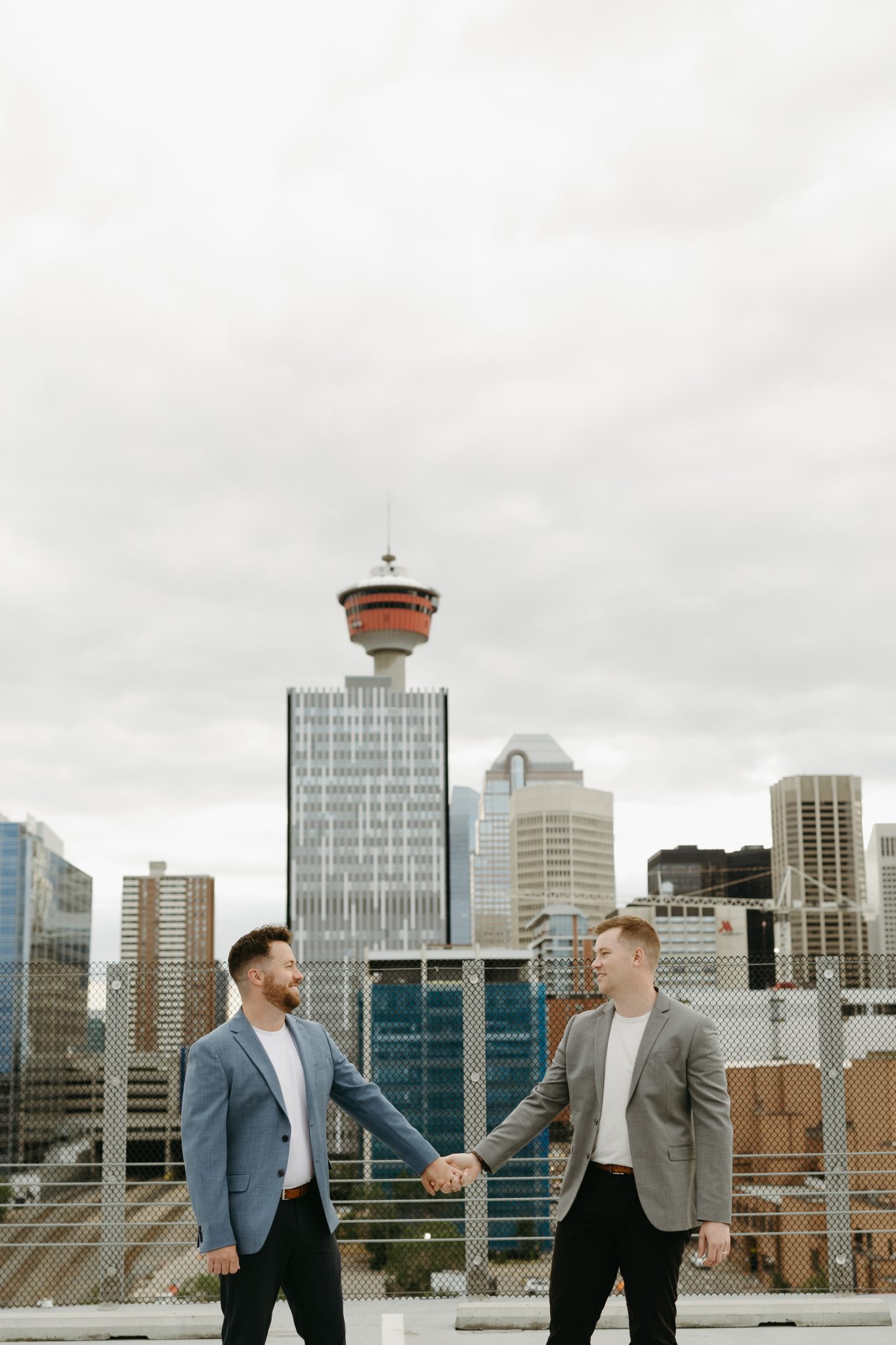 Couple holding hands on a rooftop with Alberta’s cityscape as the backdrop during their cozy engagement session.