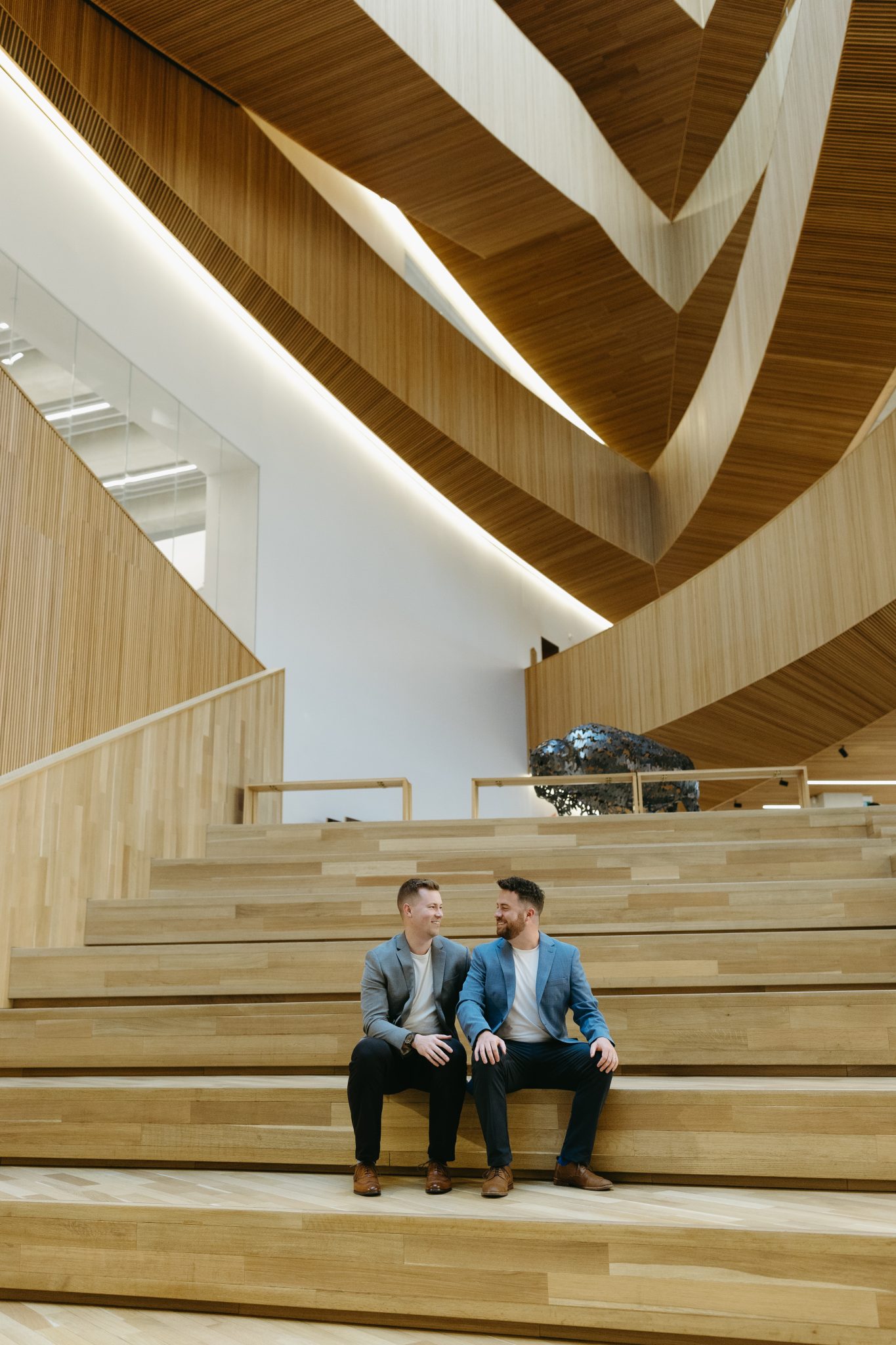 Engaged couple sitting on wooden steps in a modern indoor space for their cozy Alberta engagement session.