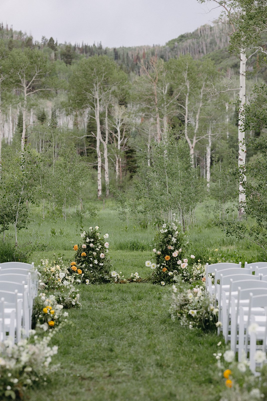 Outdoor ceremony setup with vibrant floral displays against a backdrop of Colorado mountains and aspen trees at an elevated summer wedding.