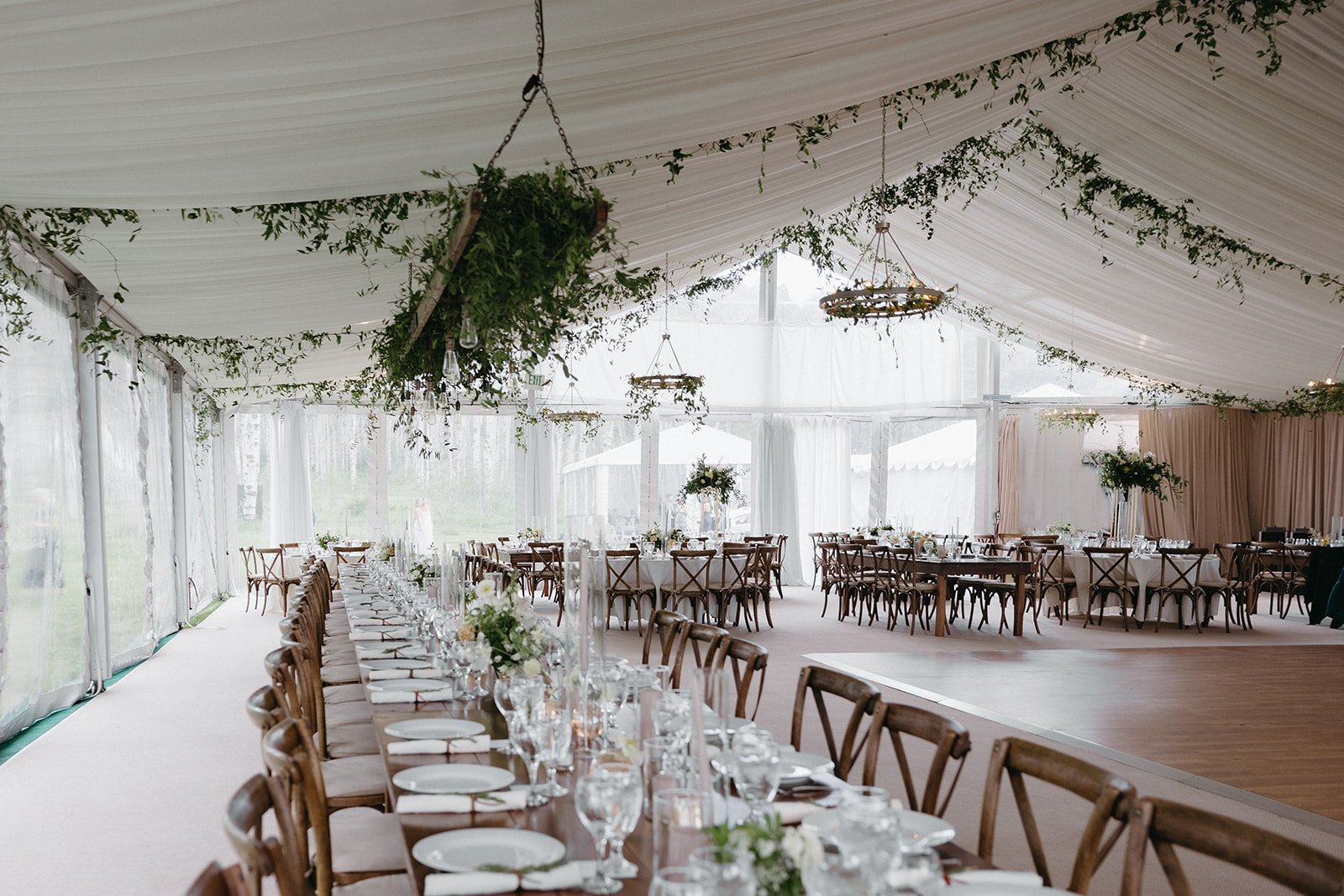 Elegant reception tent with greenery chandeliers and long tables set for guests at an elevated summer Colorado wedding.