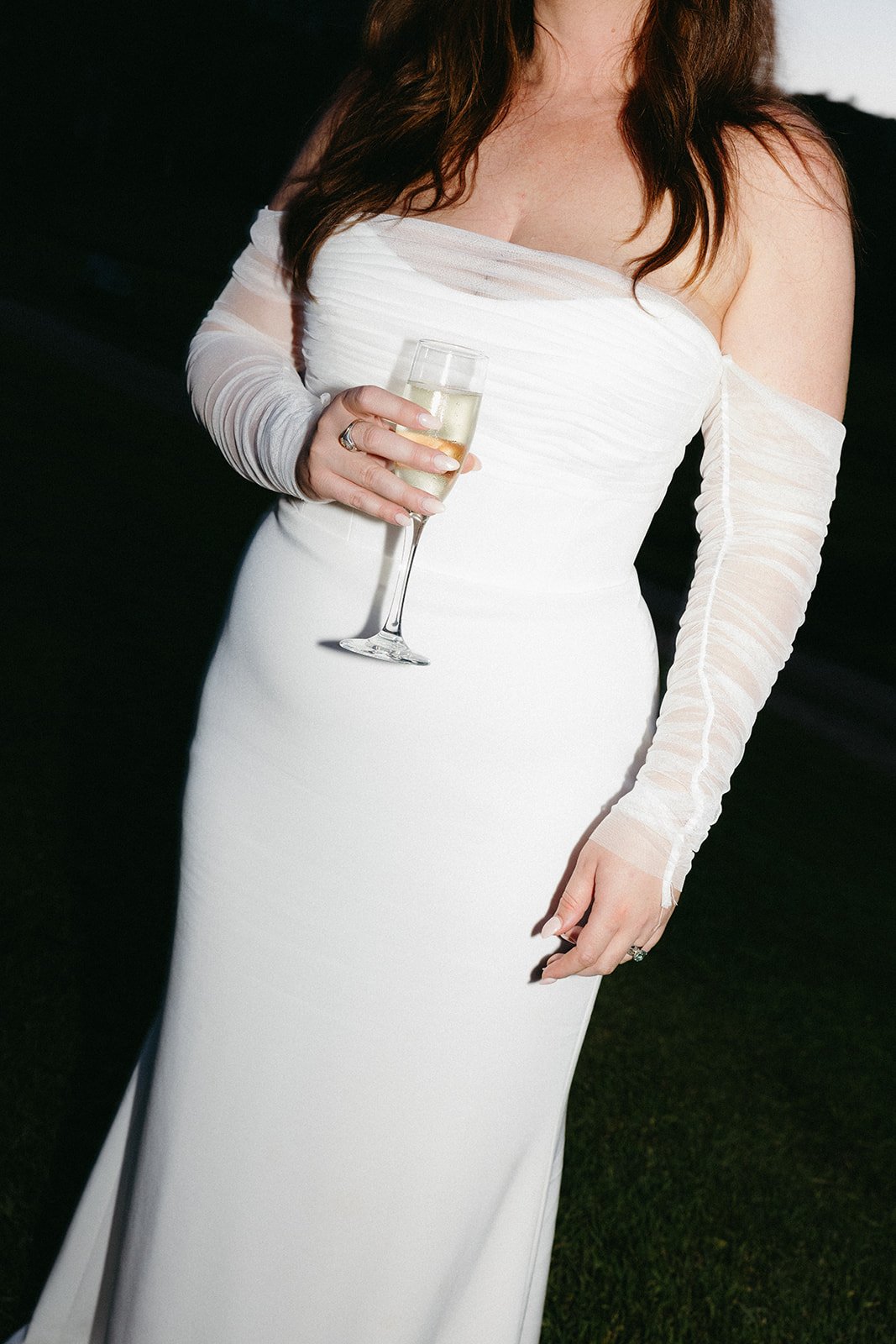 Bride holding a champagne glass in a strapless gown with sheer sleeves at an elevated summer Colorado wedding.