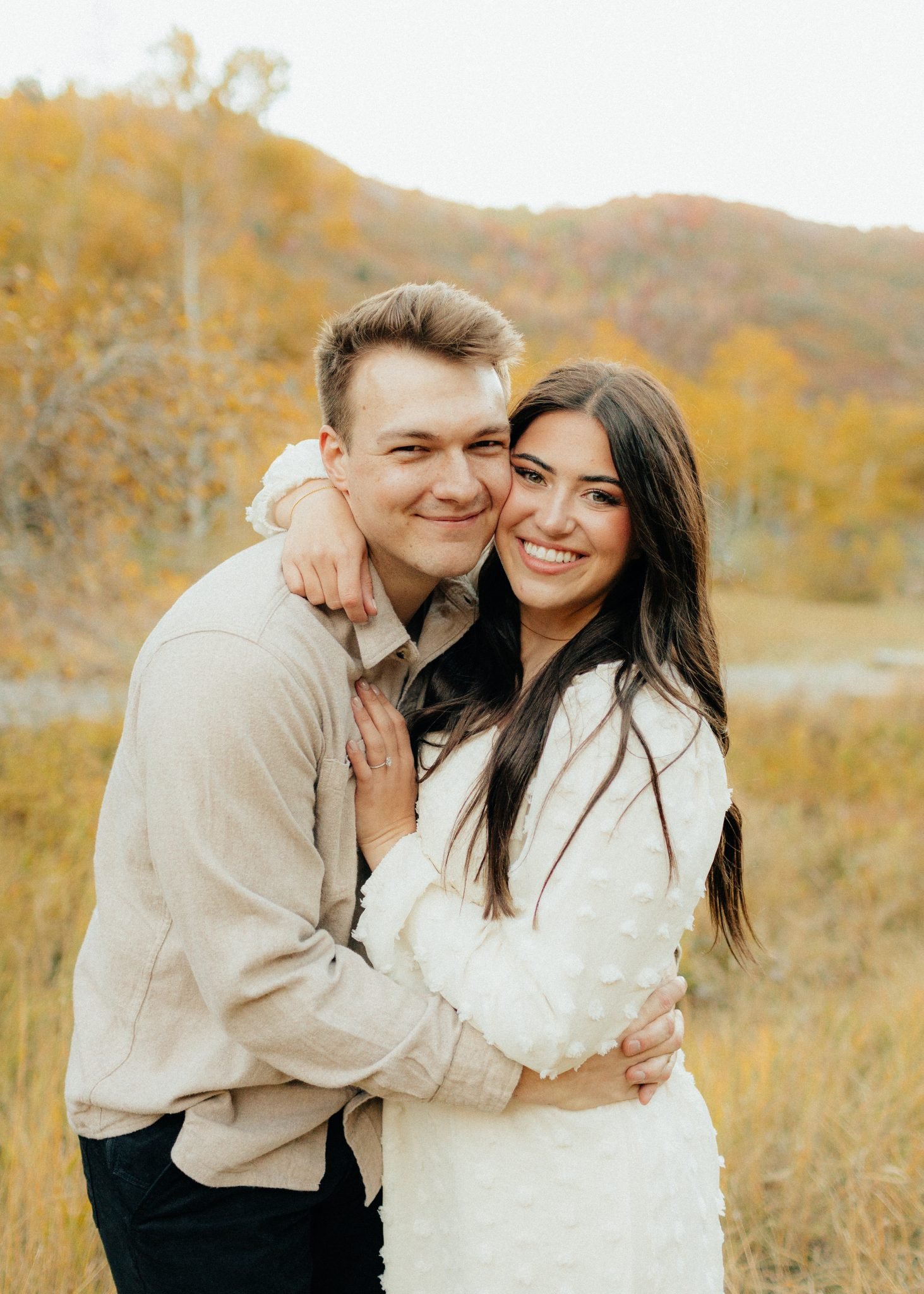 Smiling couple embracing in a fall Utah engagement session with vibrant autumn foliage in the background.