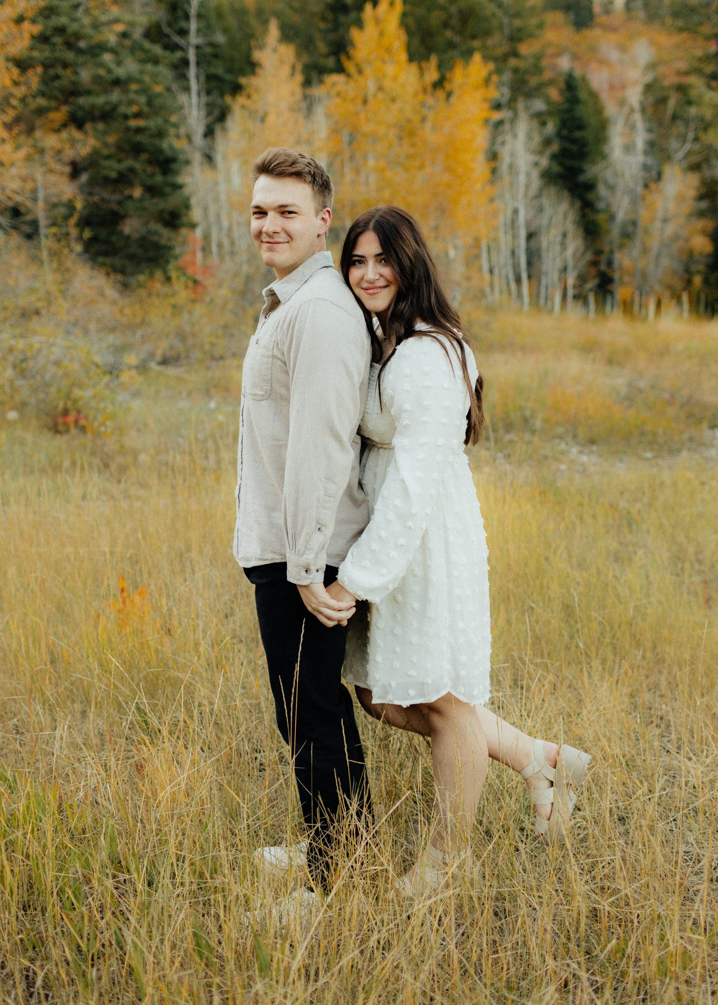 Playful couple standing in a golden field, holding hands, capturing the essence of fall Utah engagements.